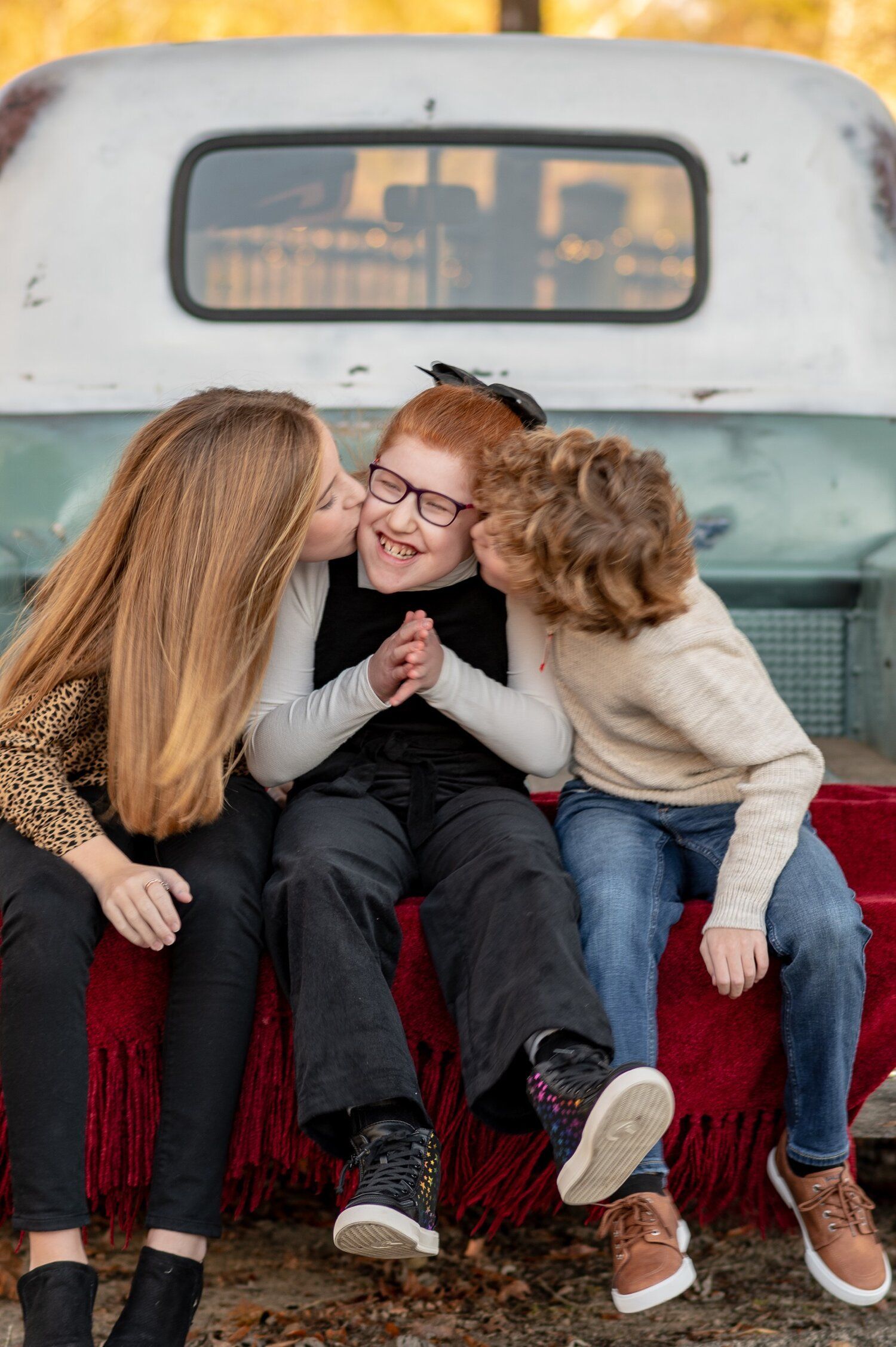 Three children are sitting on the back of a truck.