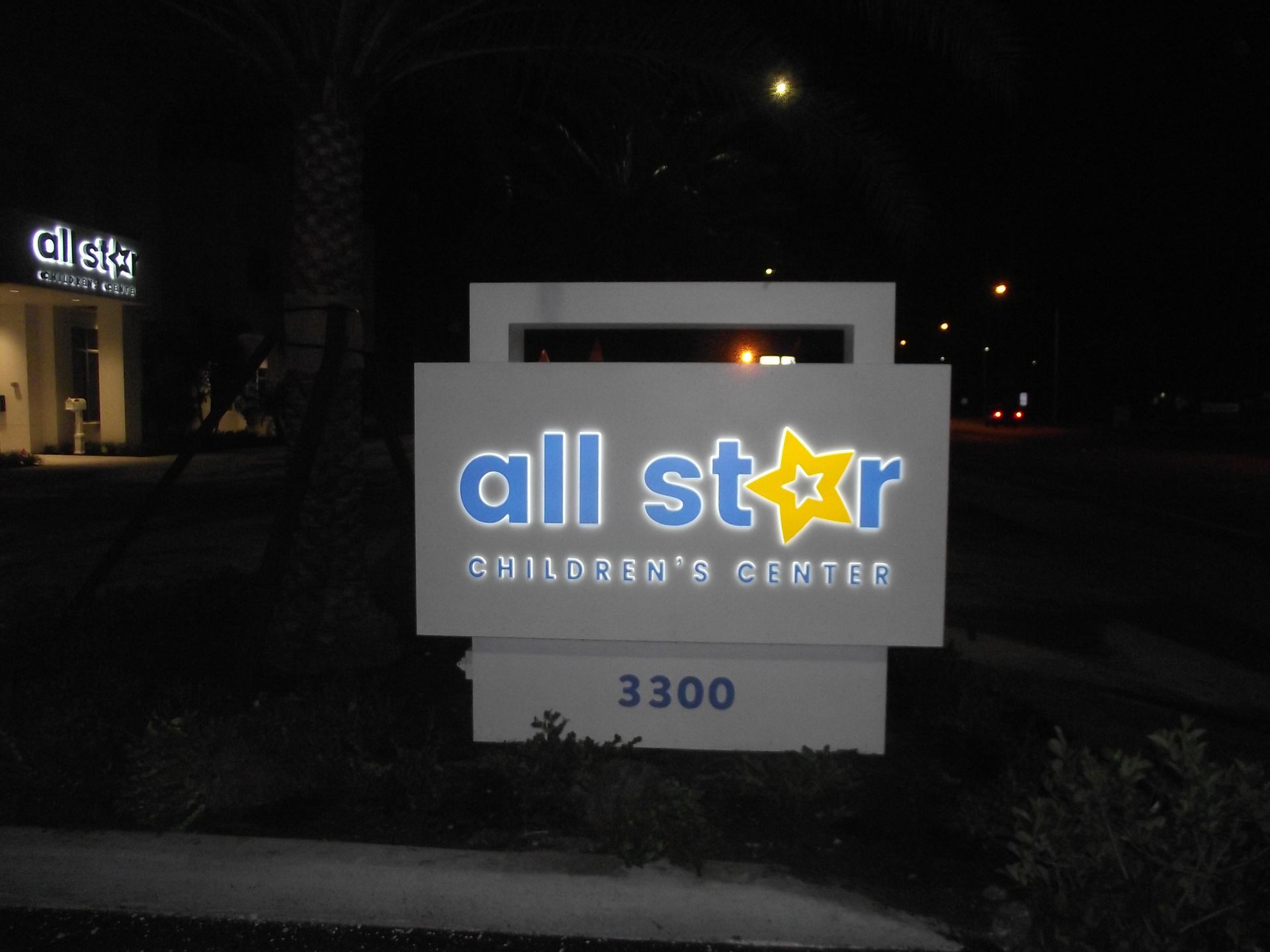 Illuminated sign for All Star Children's Center at night, with blue lettering and a yellow star. The address 3300 is below.