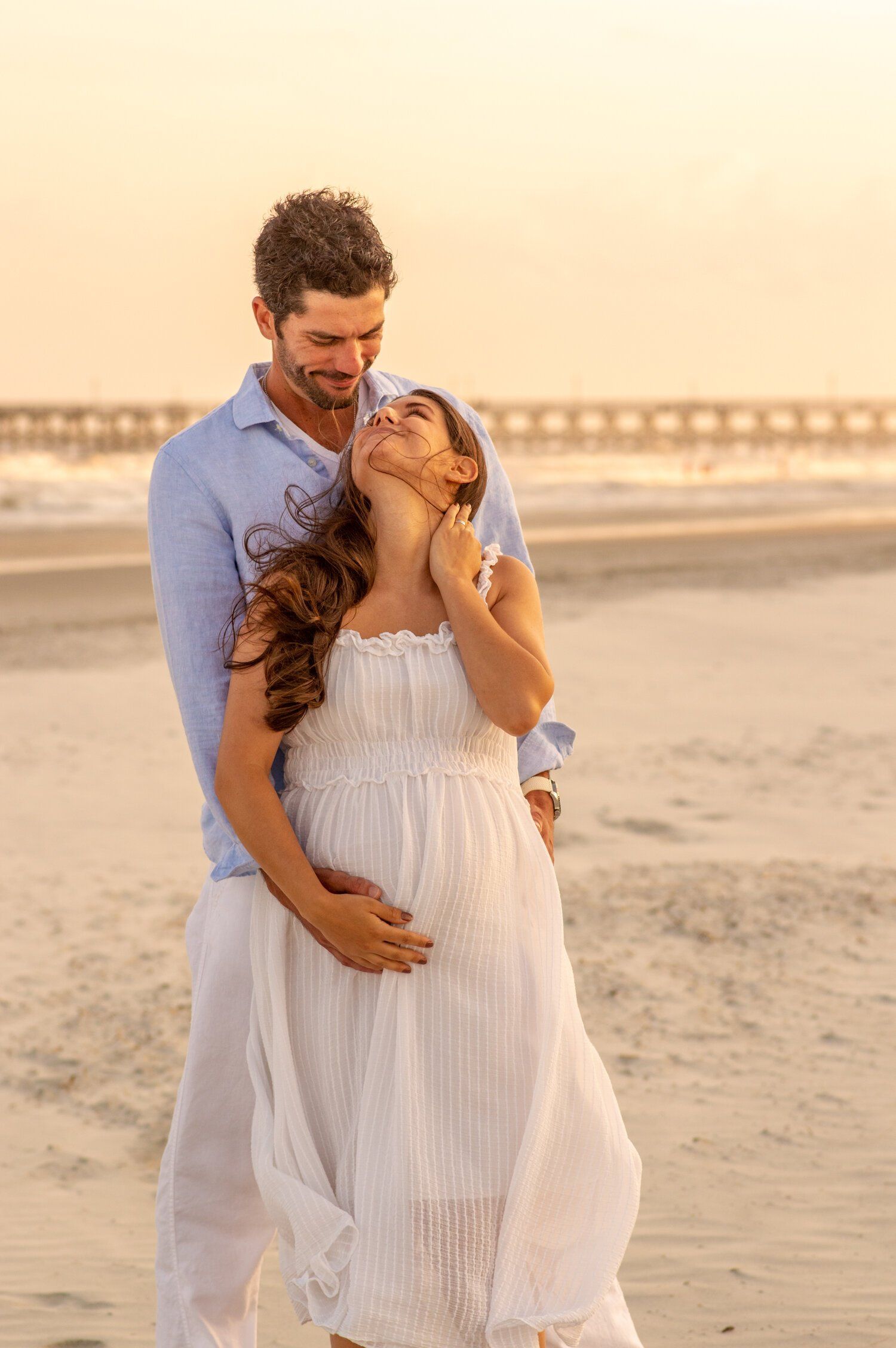 A man is hugging a pregnant woman on the beach.