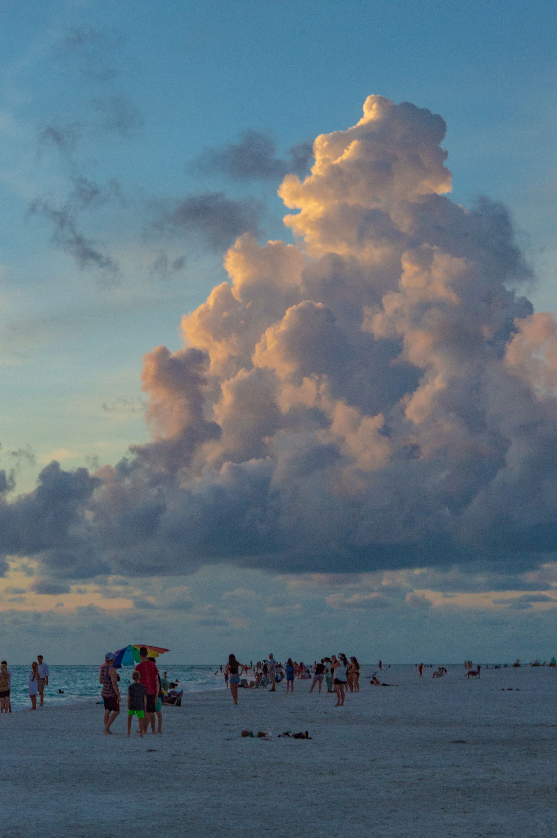 A group of people are standing on a beach with a large cloud in the sky.