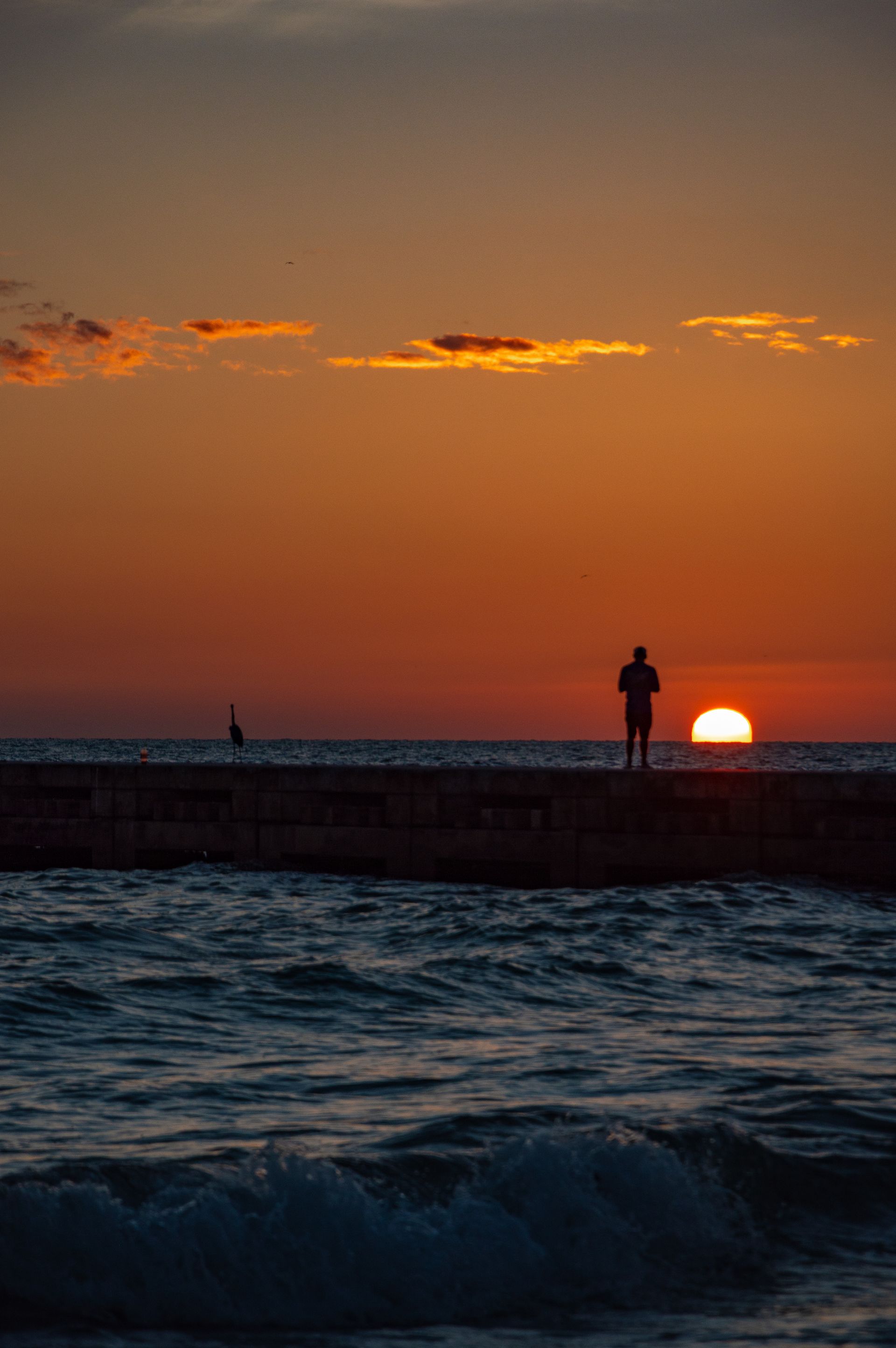 A man is standing on a pier overlooking the ocean at sunset.