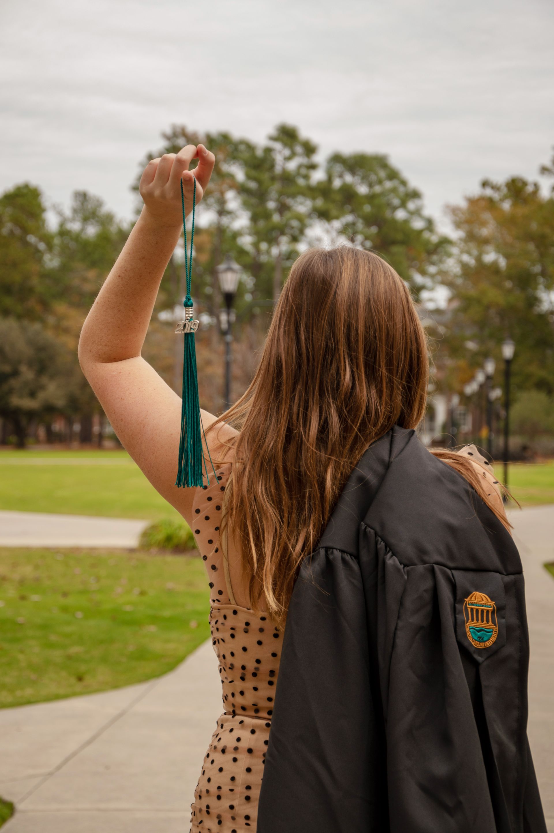 A woman in a graduation cap and gown is holding a tassel over her head.