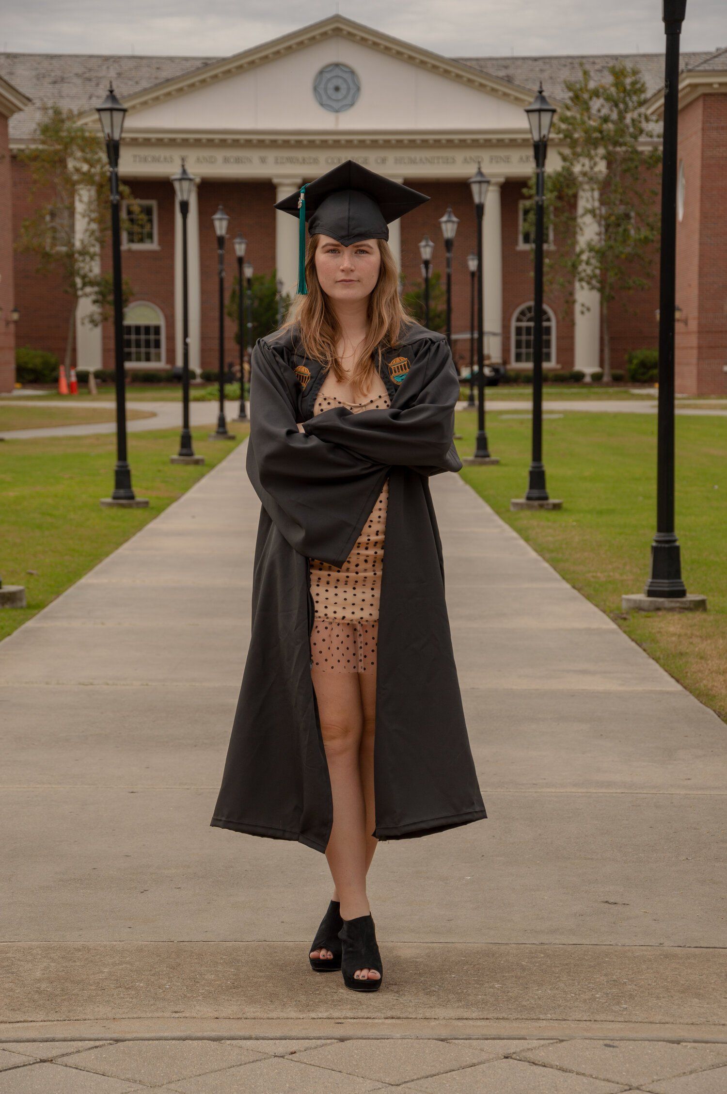 A woman in a graduation cap and gown is standing on a sidewalk in front of a building.