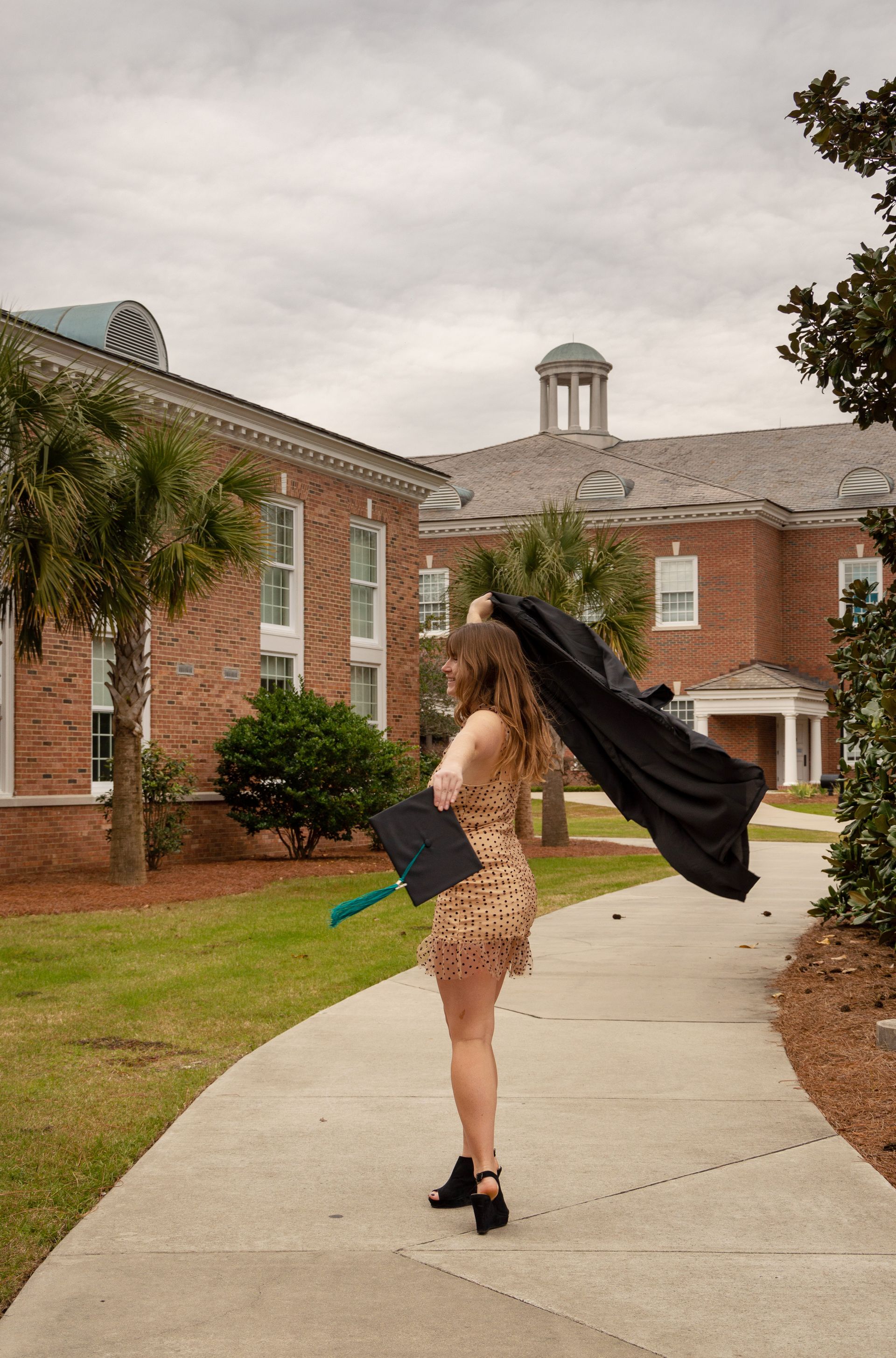 A woman is standing on a sidewalk holding a graduation cap and gown.