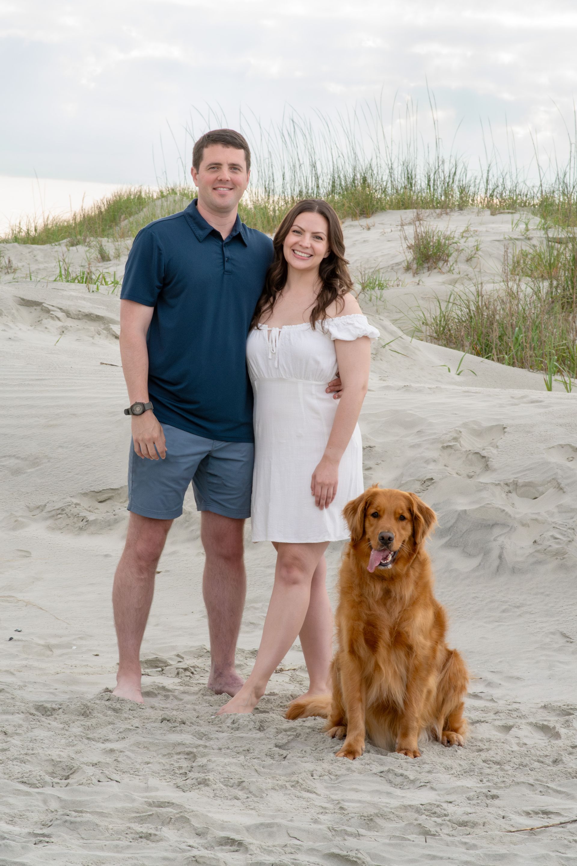 A man and a woman are posing for a picture with their dog on the beach.