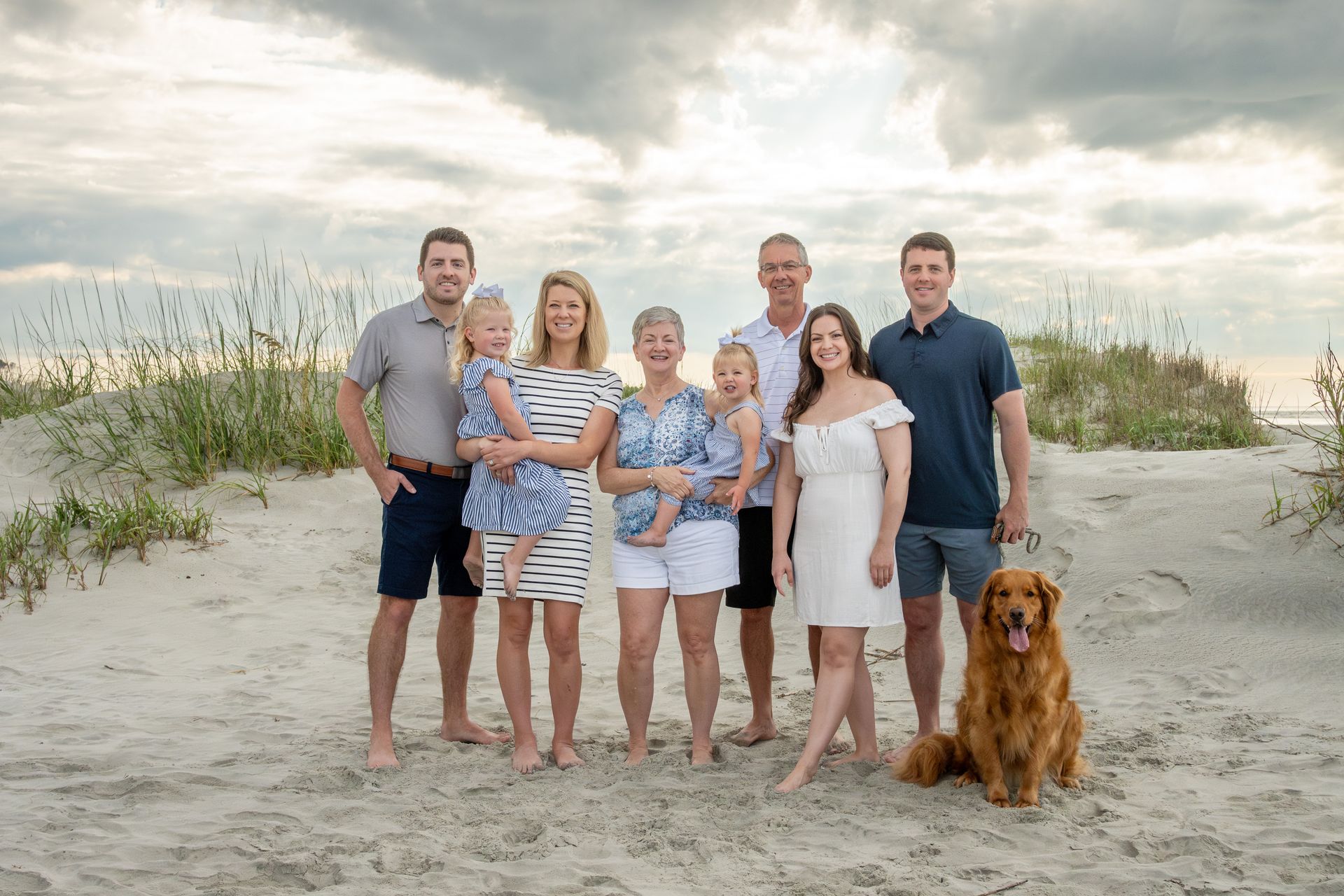 A large family is posing for a picture on the beach with a dog.