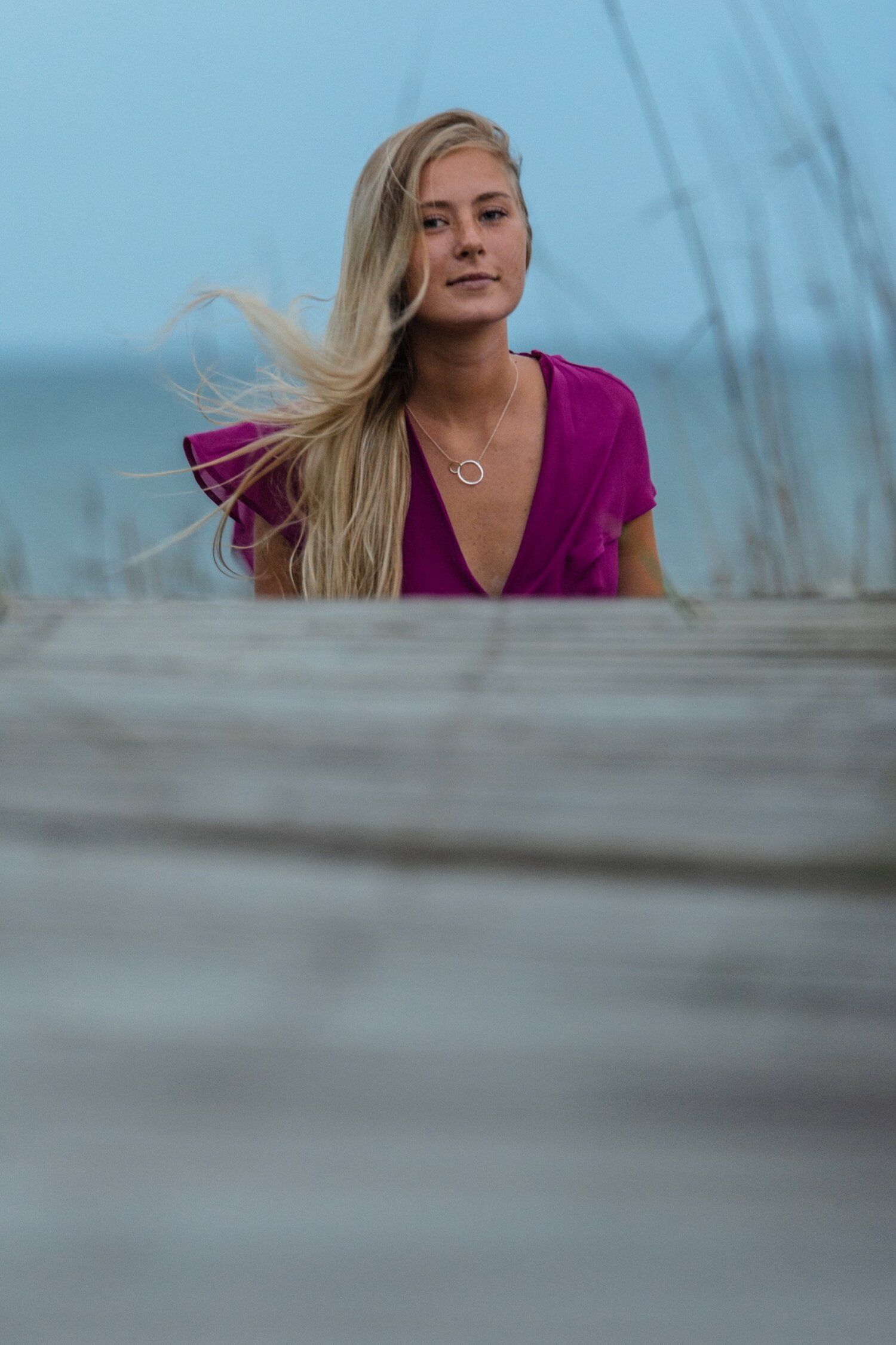 A woman in a purple dress is standing on a pier near the ocean.
