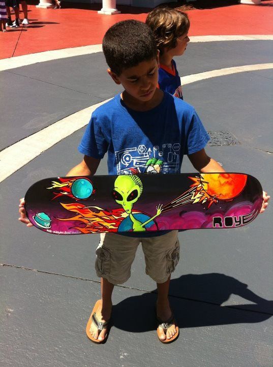 A young boy is holding a skateboard with an alien on it