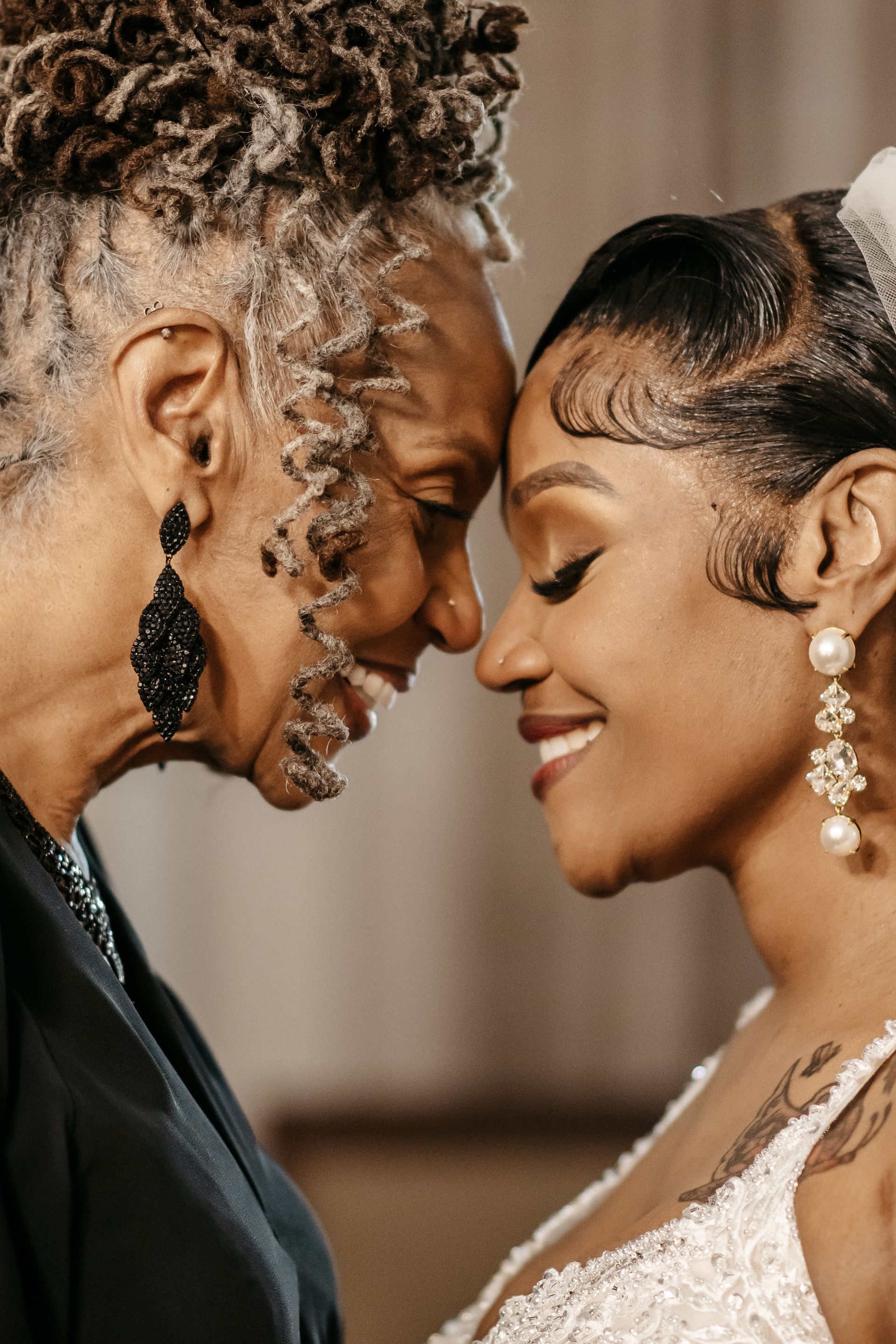 A bride and her mother are looking at each other and smiling.