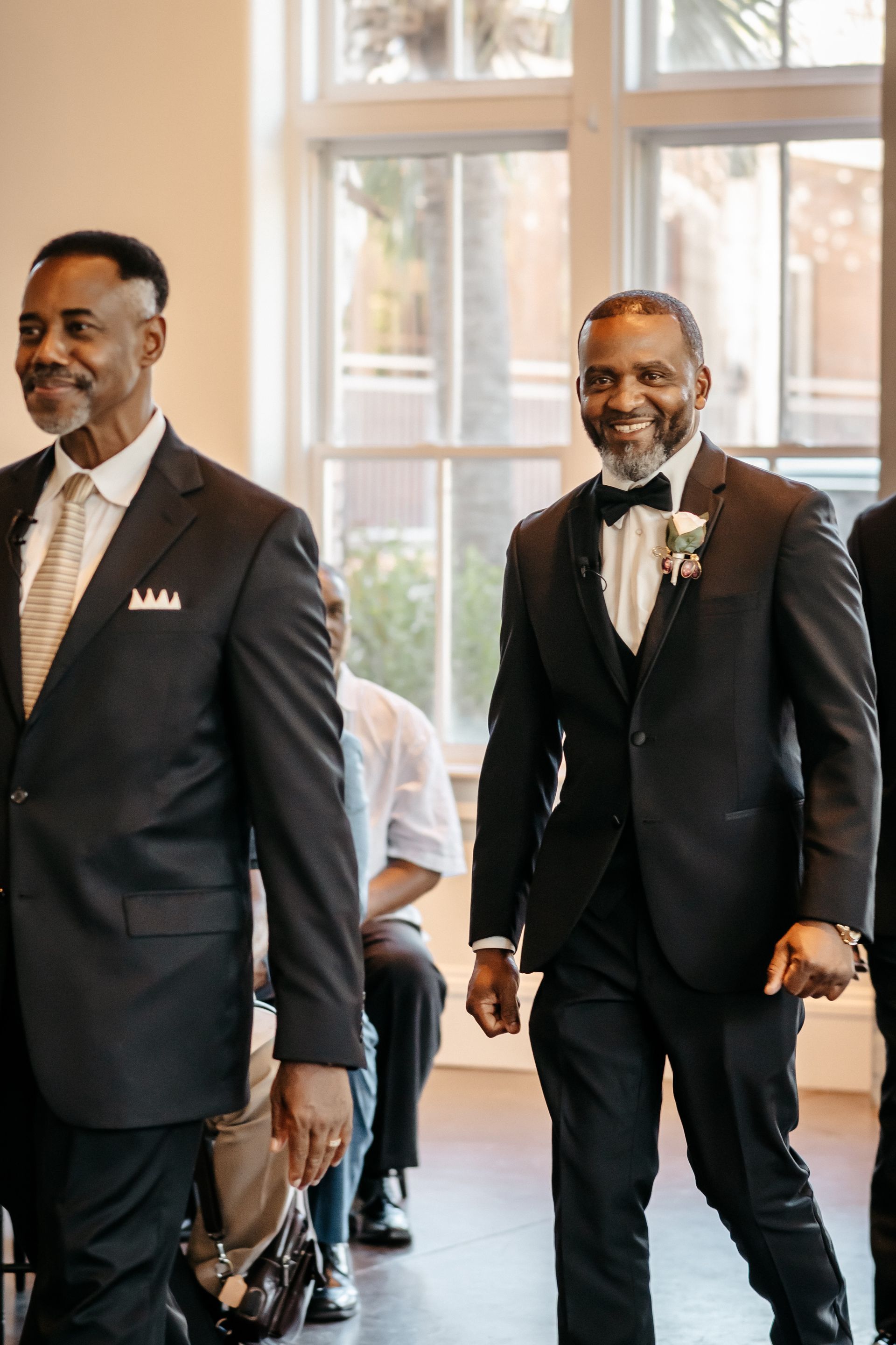 Two men in suits are walking down the aisle at a wedding.