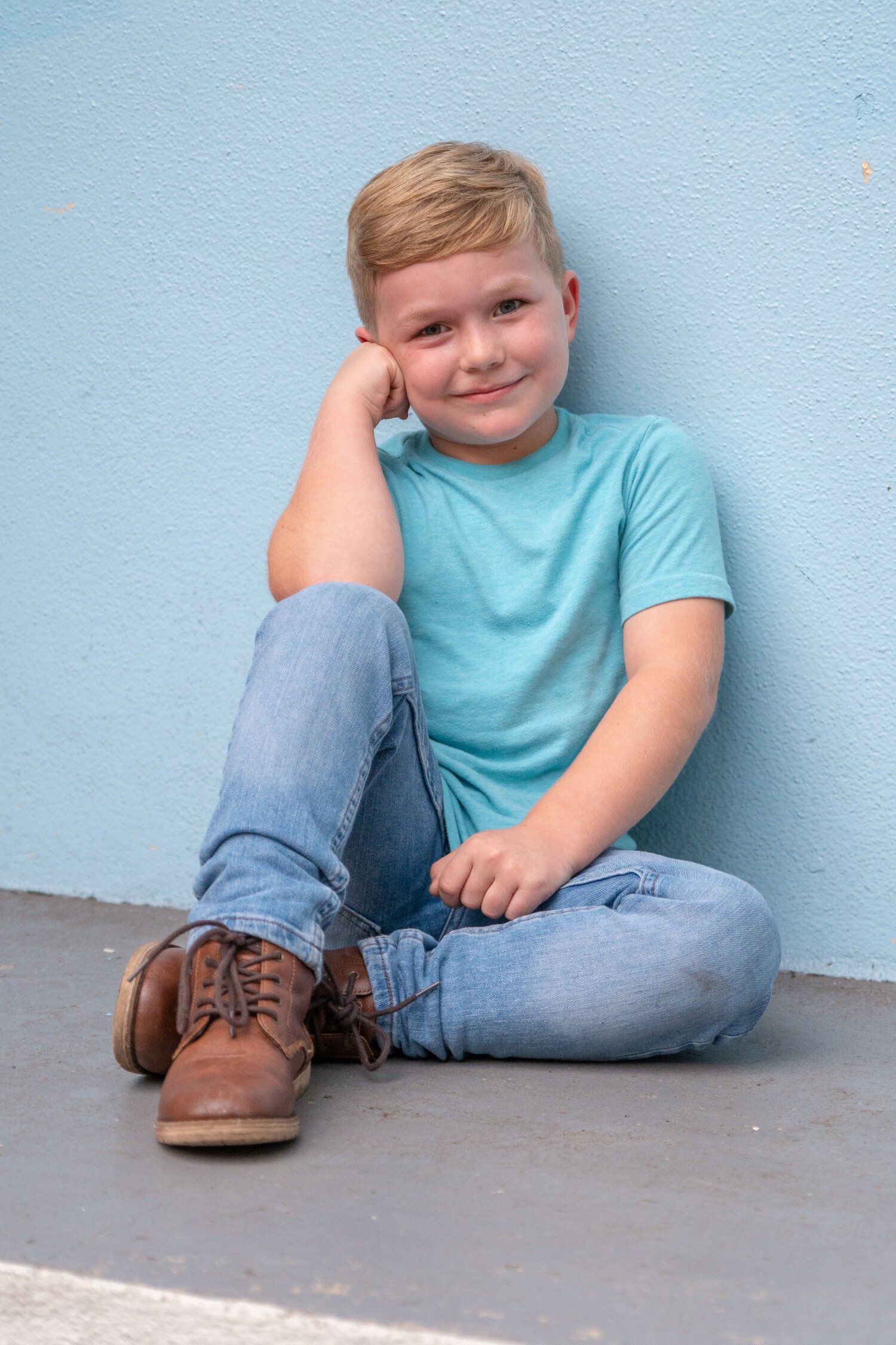 A young boy is sitting on the ground in front of a blue wall.
