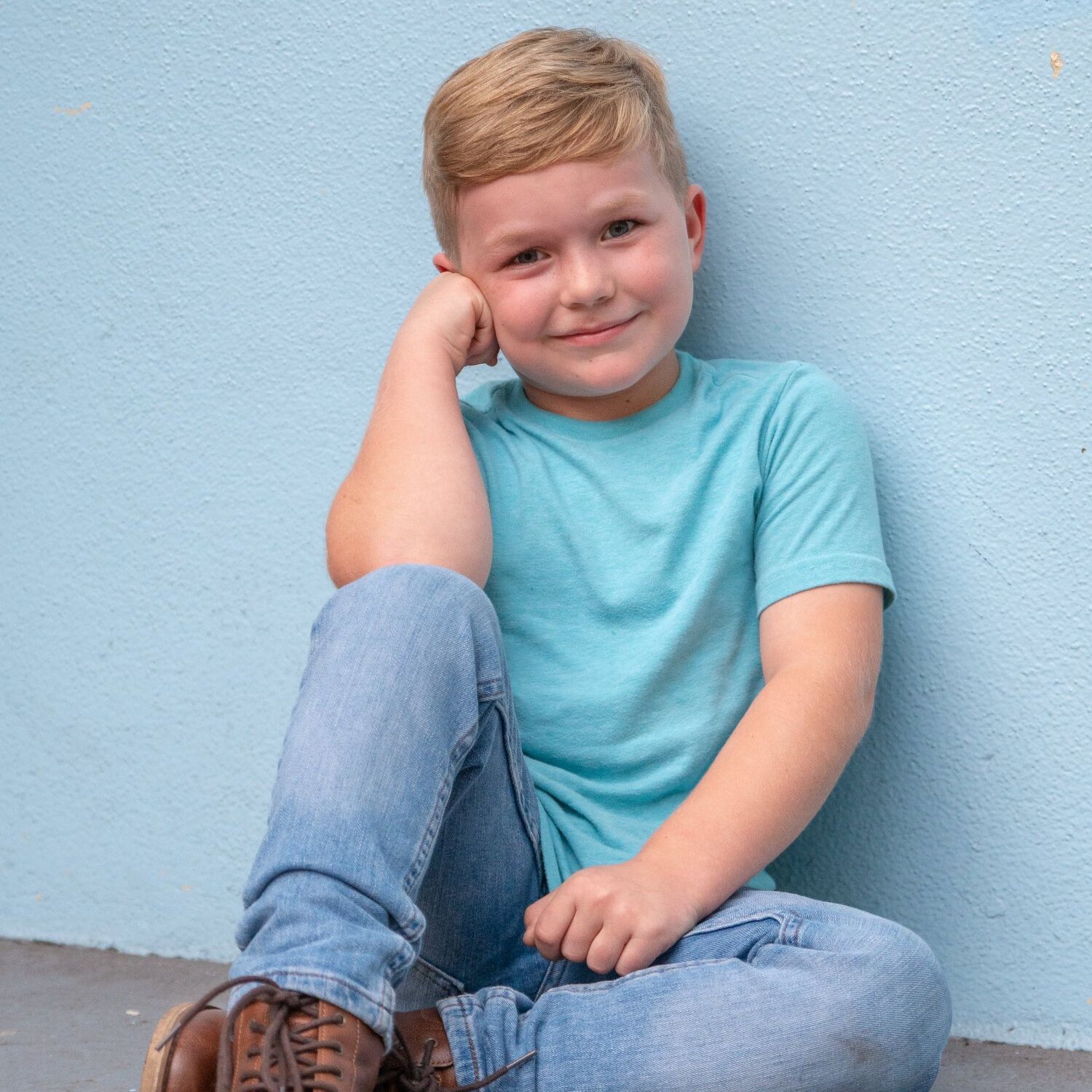 Young boy photo sitting against the wall in a blue shirt with blue eyes