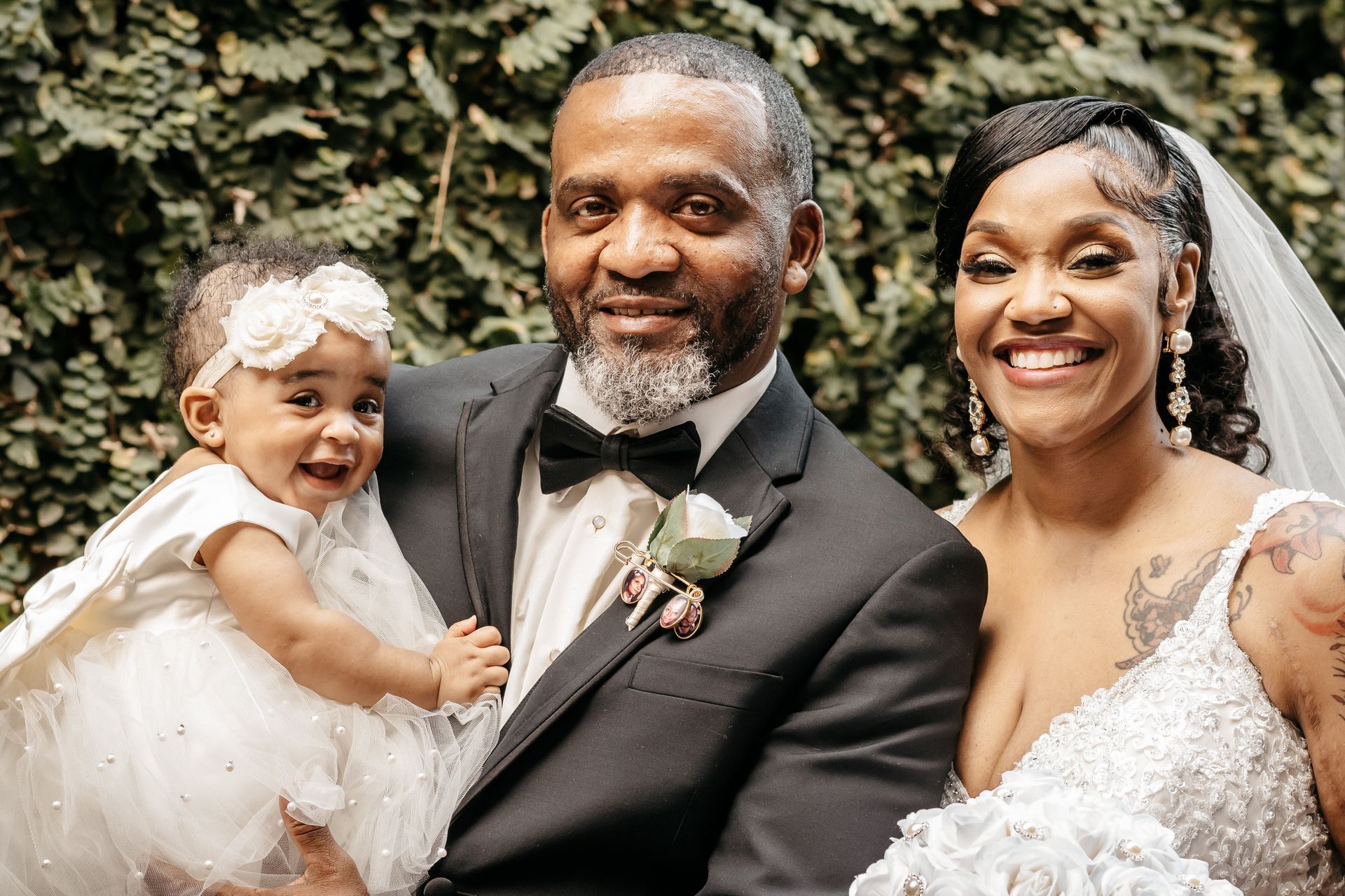 A bride and groom are posing for a picture with a baby girl.