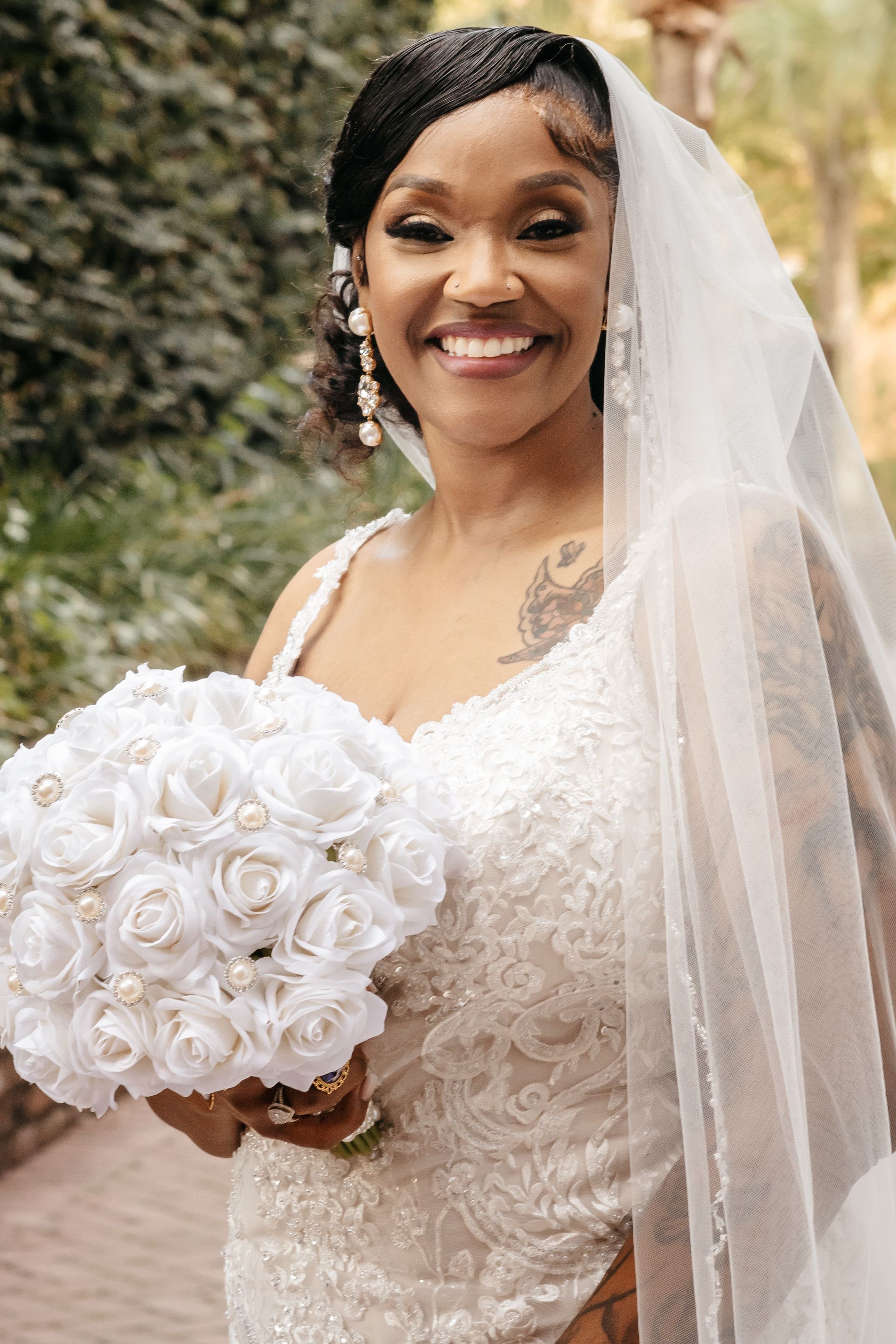 A bride in a wedding dress is holding a bouquet of white roses and smiling.