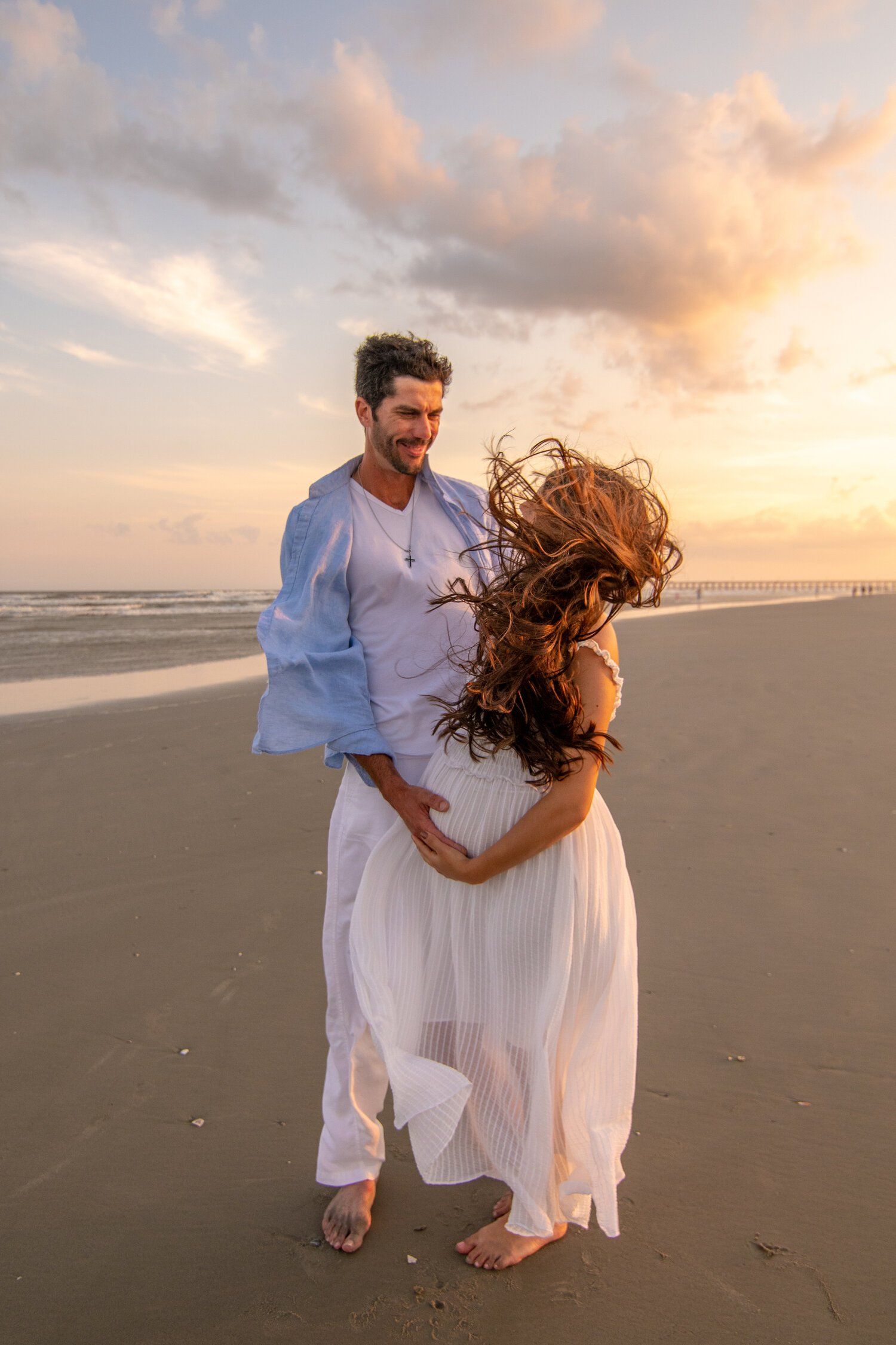 A man and a woman are standing on a beach at sunset.