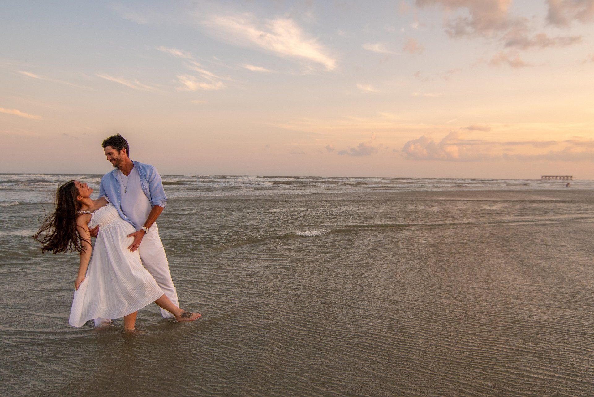 A man is holding a woman in his arms while walking on the beach.