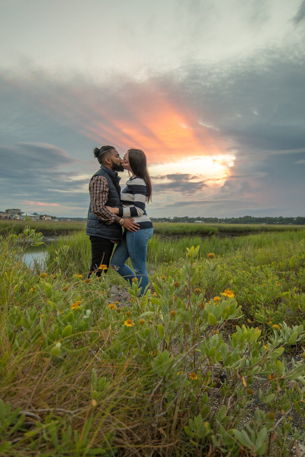 A man and a woman are kissing in a field at sunset.