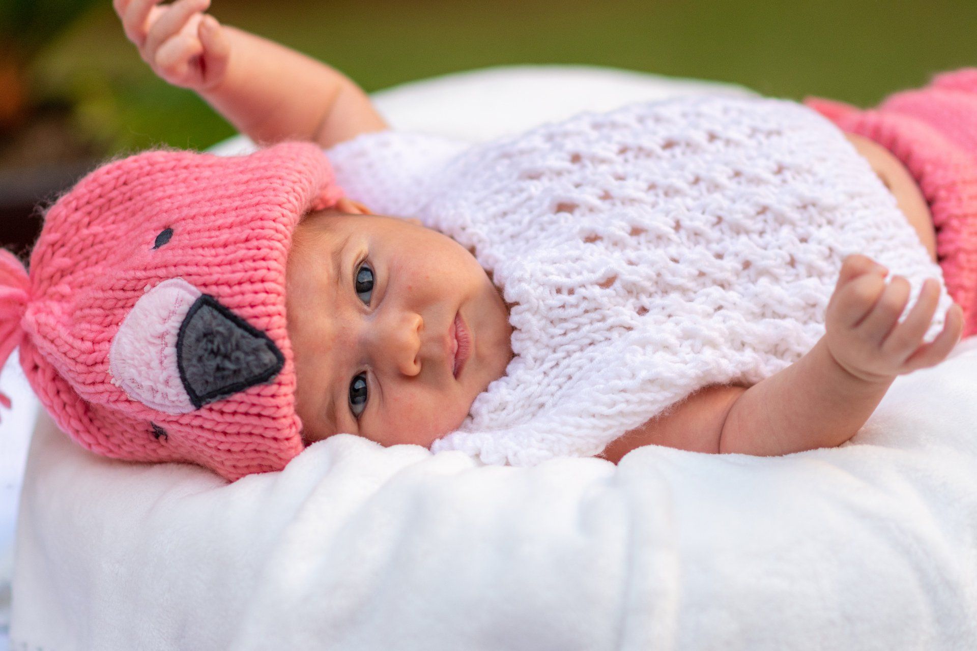 A baby is wearing a pink flamingo hat and laying on a pillow.