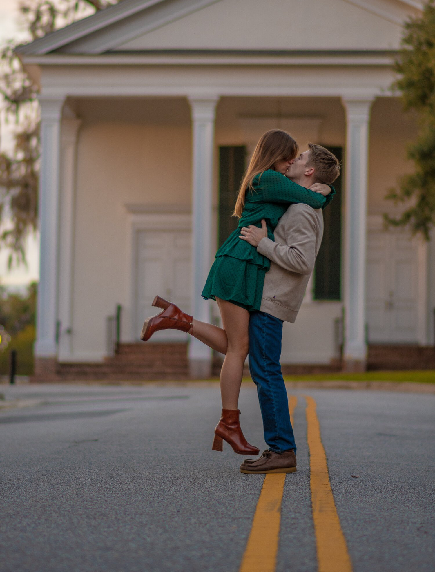 A man is holding a woman in his arms and kissing her in front of a building.