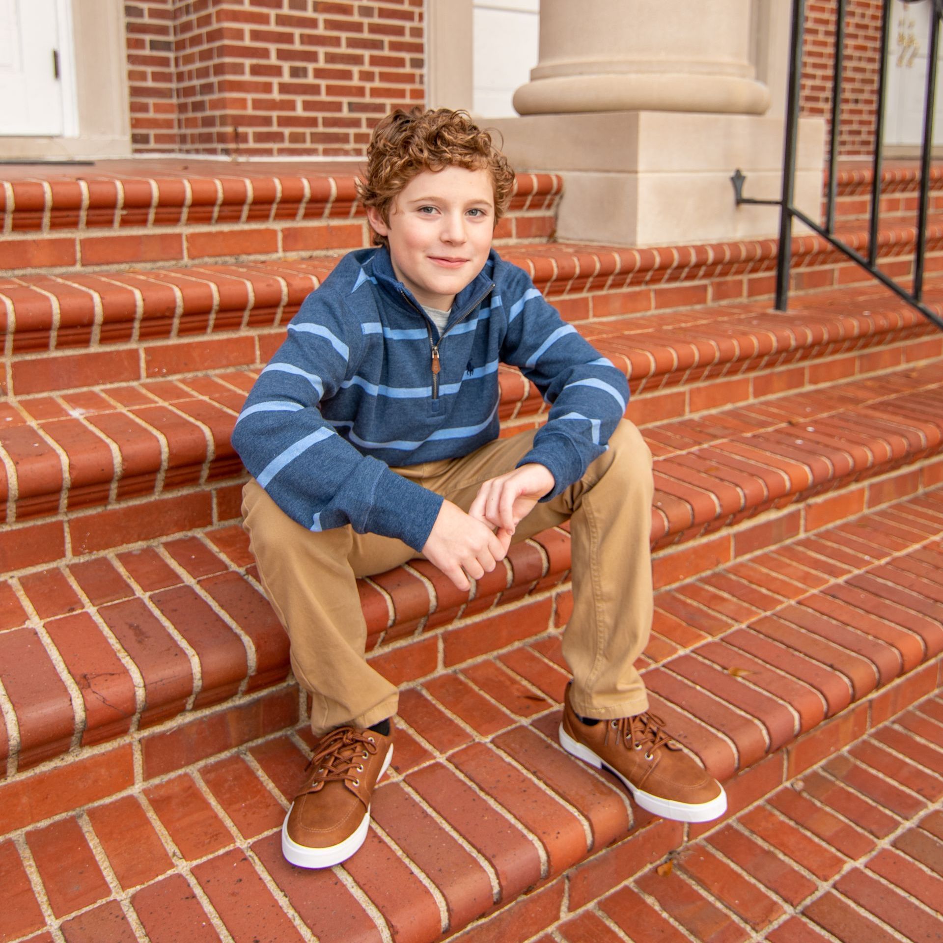 A young boy is sitting on a set of brick steps
