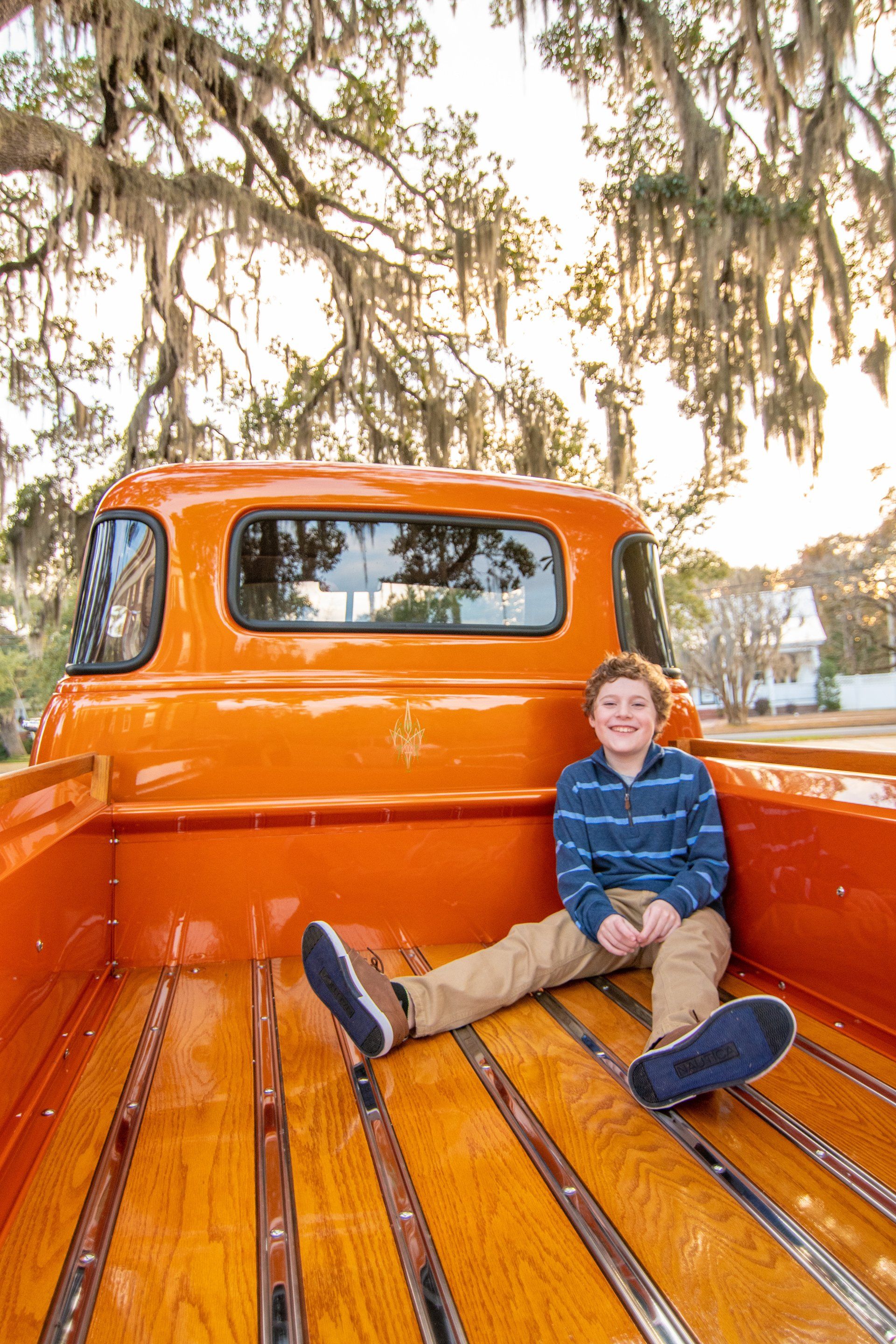 A young boy is sitting in the back of an orange truck.