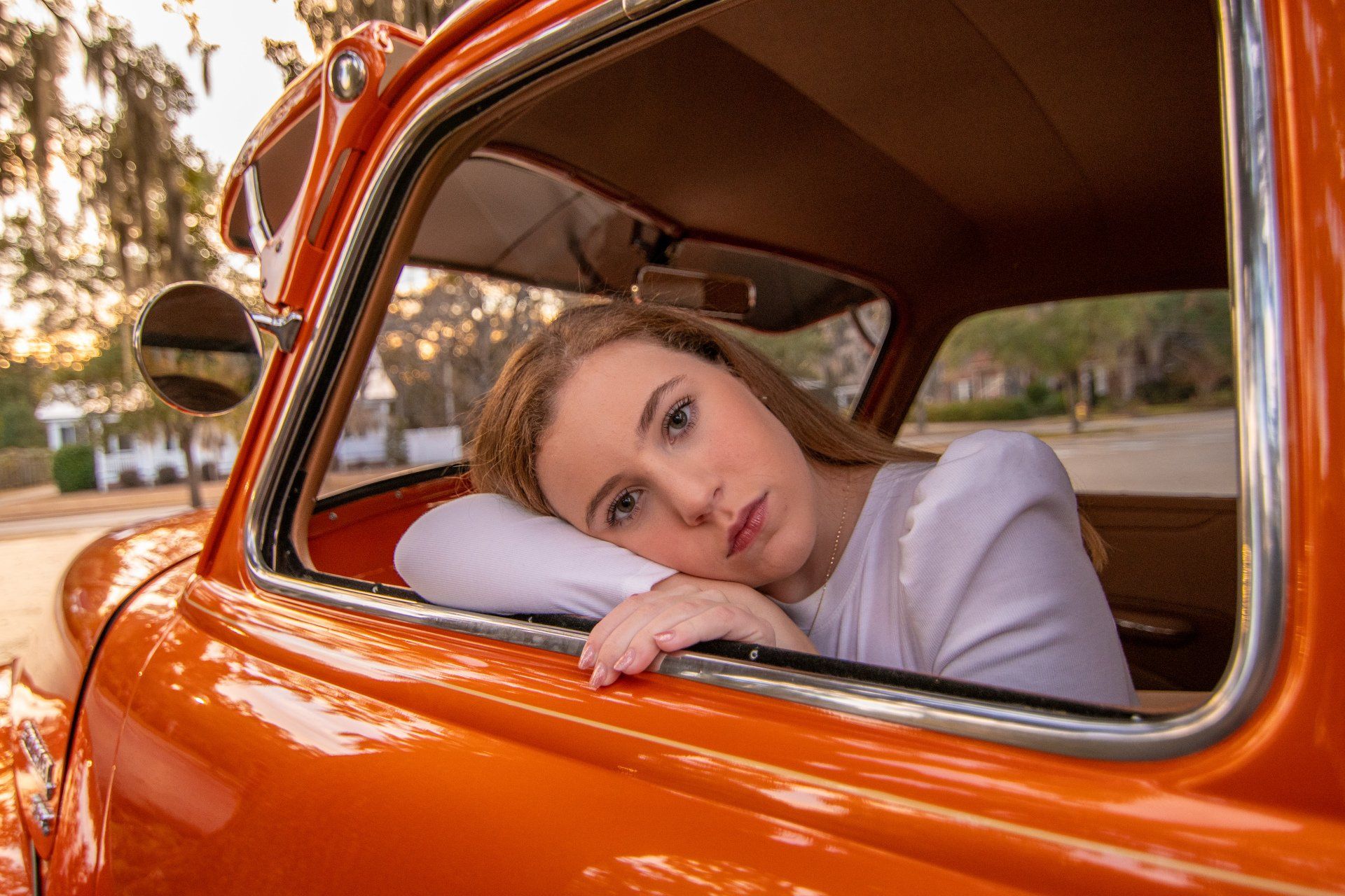 A woman is leaning her head out of the window of an orange car.