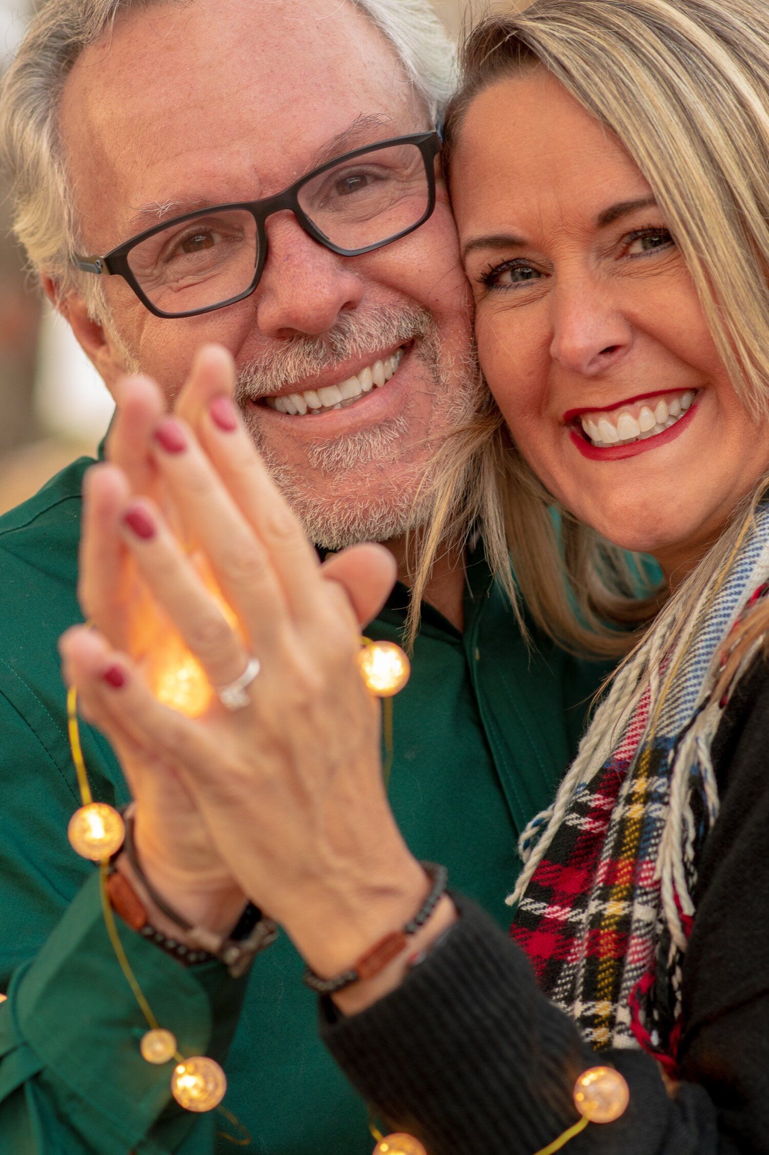 A man and a woman are posing for a picture with christmas lights in the background.