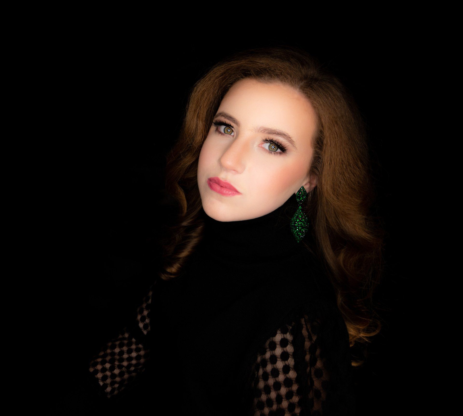 The woman is wearing a black turtleneck and green earrings.