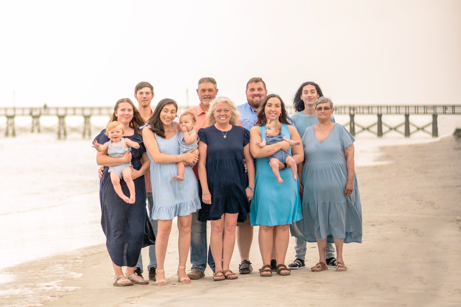 A large family is posing for a picture on the beach.
