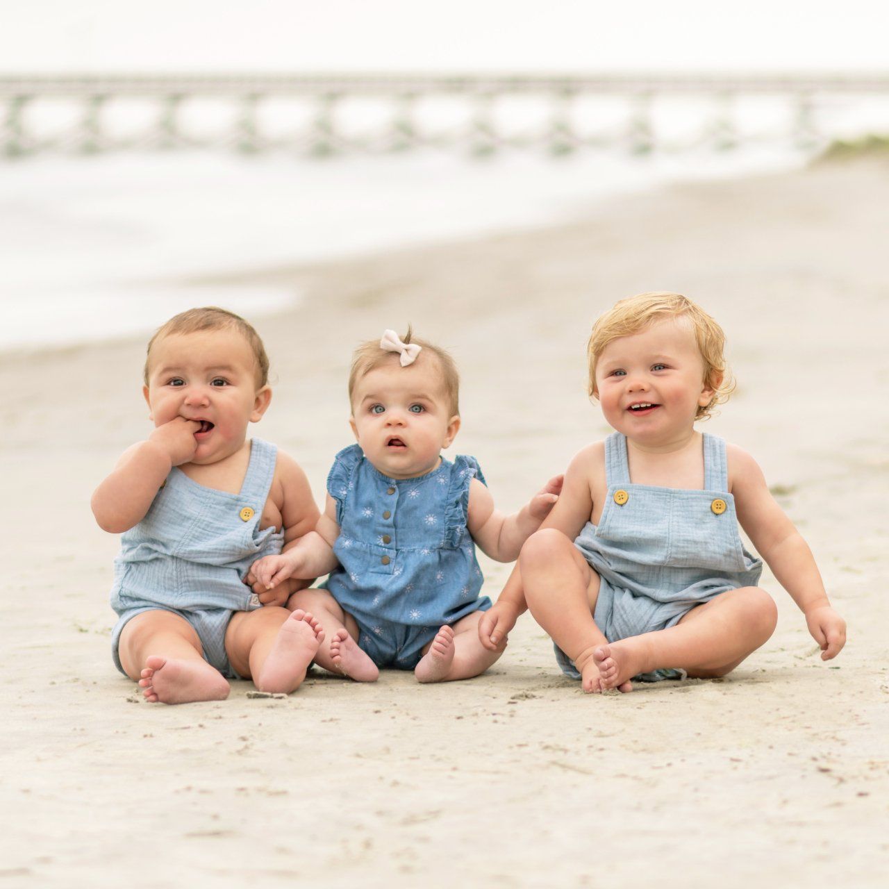 Three babies are sitting next to each other on the beach.