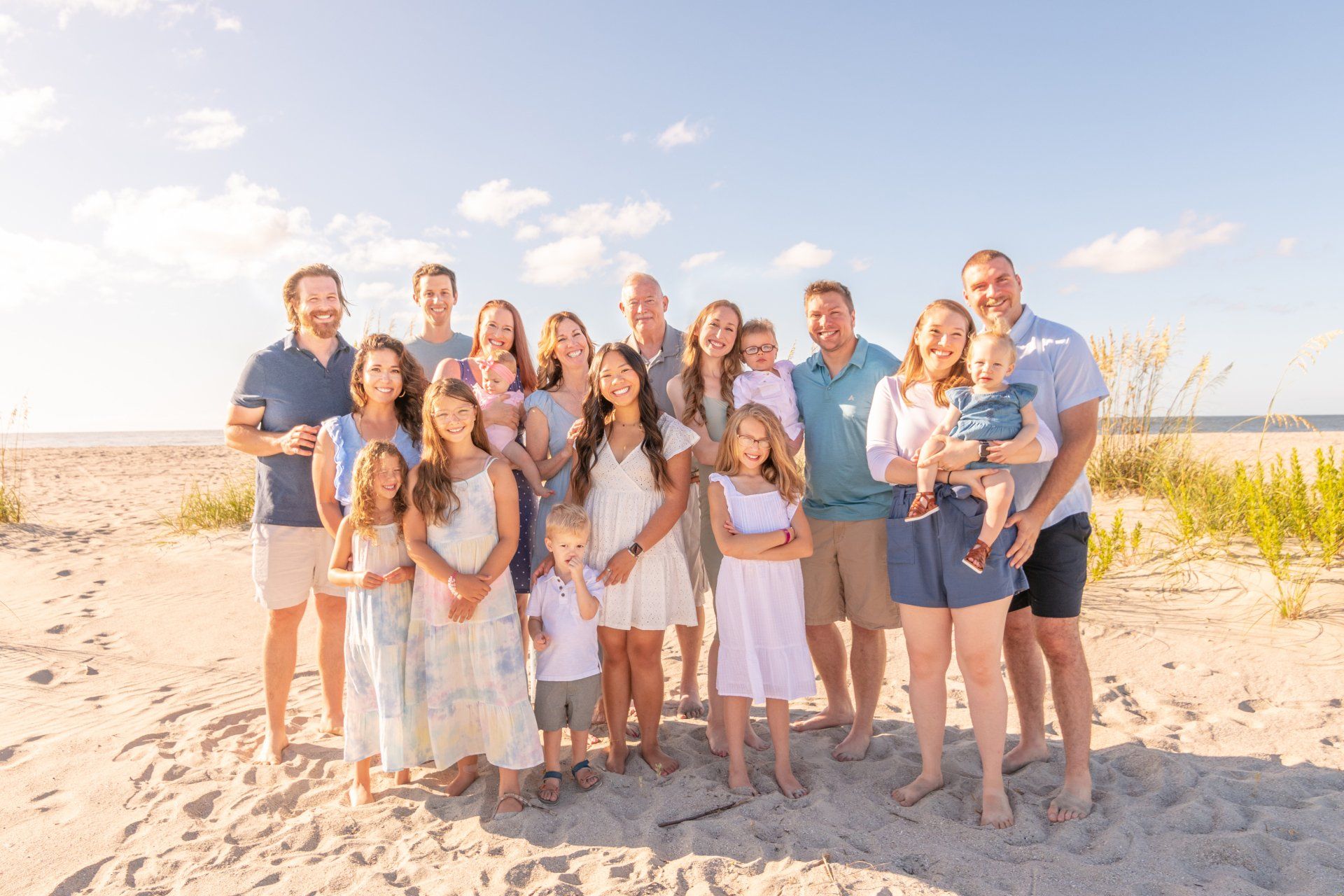 A large family is posing for a picture on the beach.