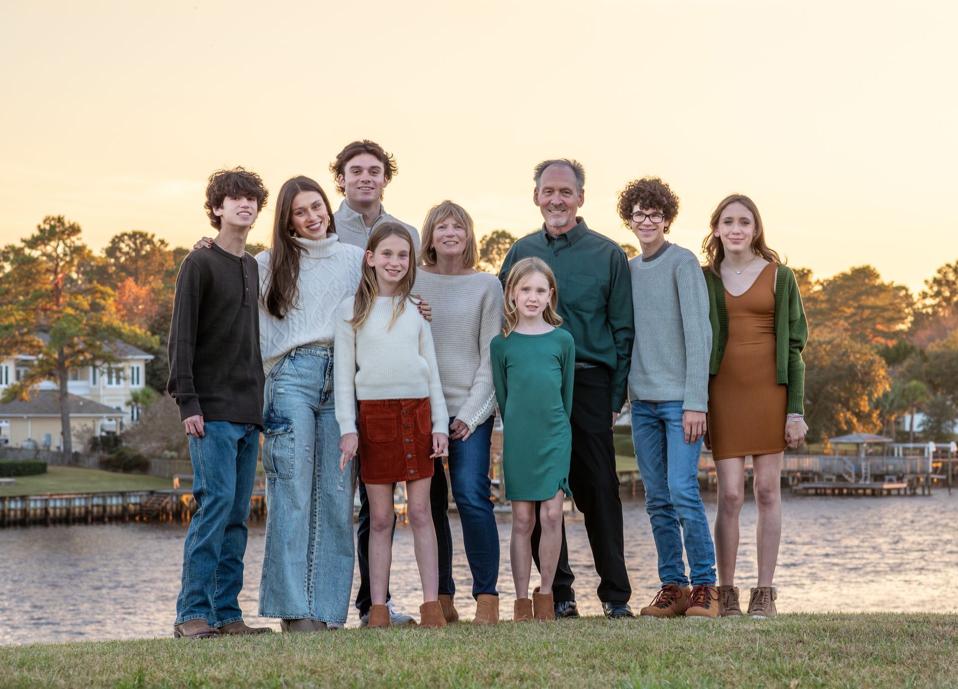 A large family is posing for a picture in front of a body of water.