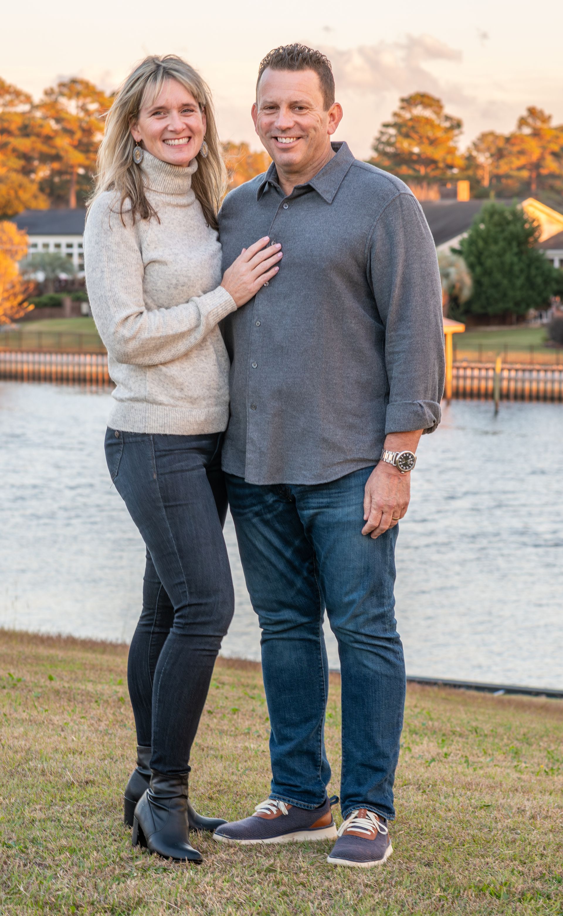 A man and a woman are standing next to each other in front of a lake.
