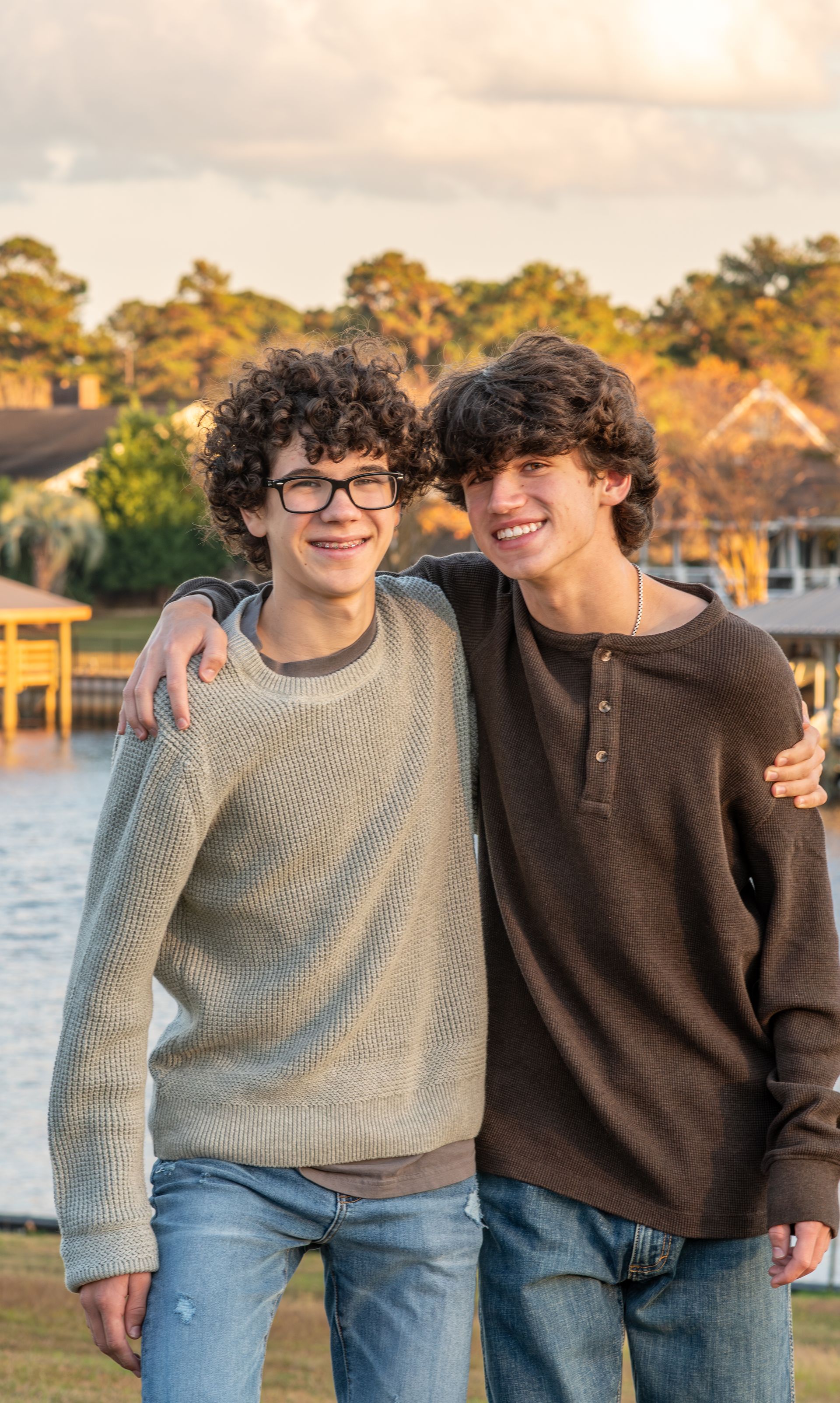 Two young men are standing next to each other in front of a body of water.