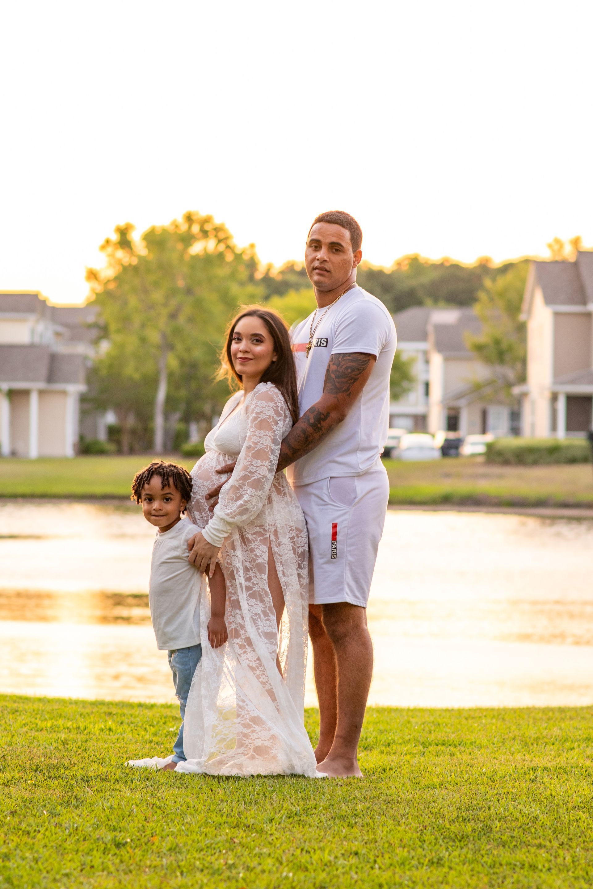 A pregnant woman is standing in the grass with her husband and son.