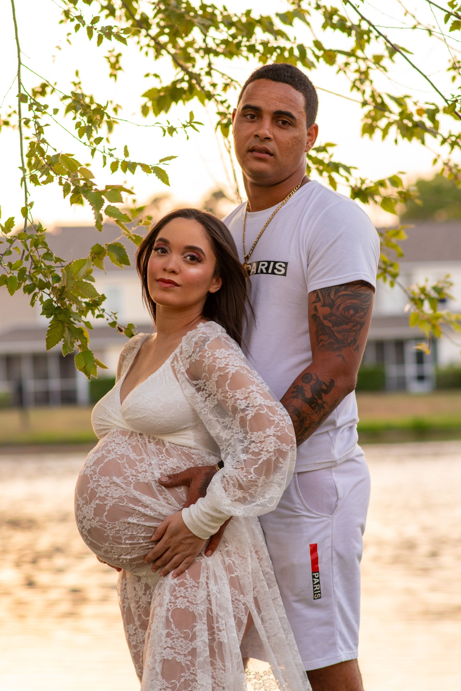 A man and a pregnant woman are standing next to each other under a tree.