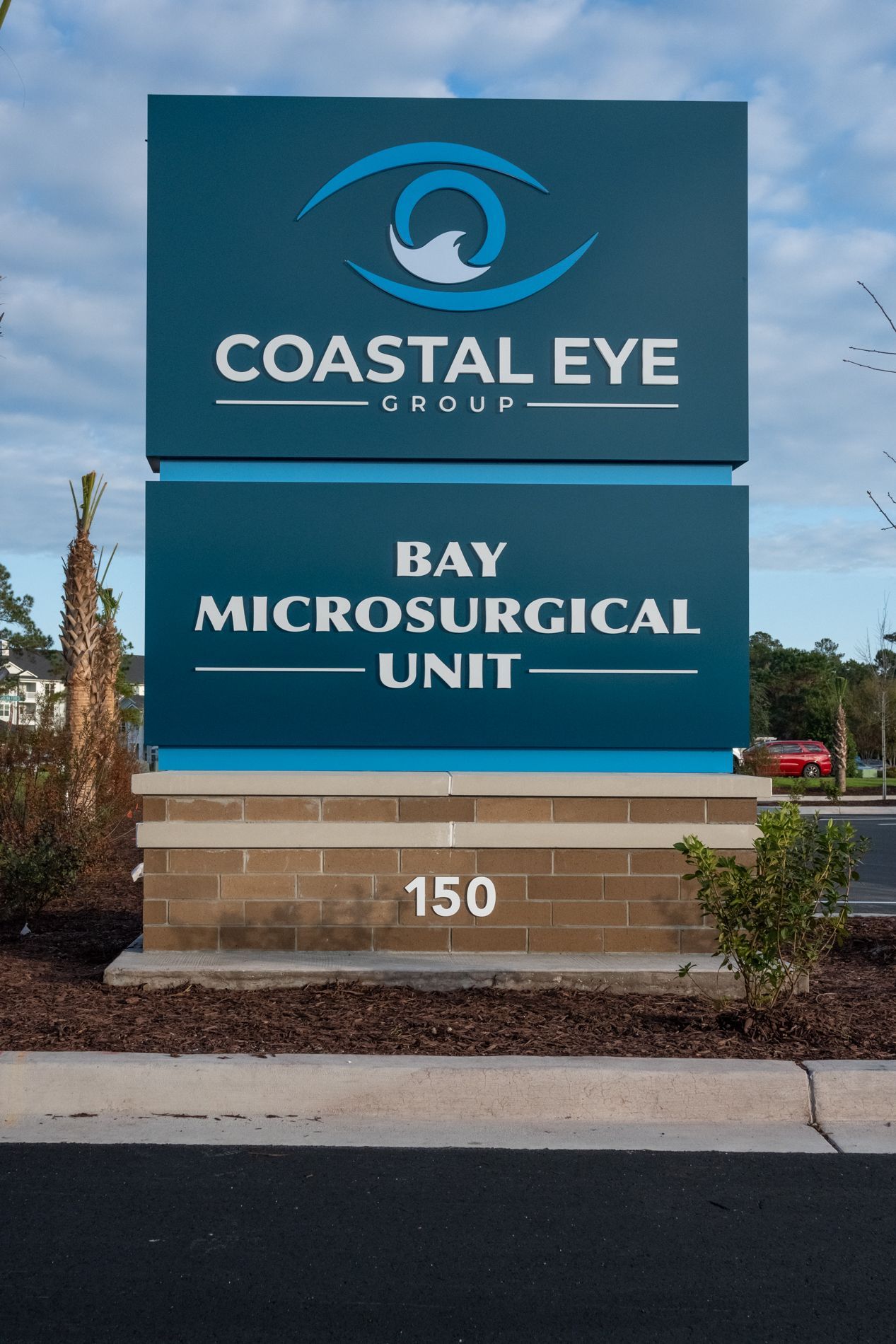 Monument sign for Coastal Eye Group and Bay Microsurgical Unit at 150, blue and white logo, teal background.