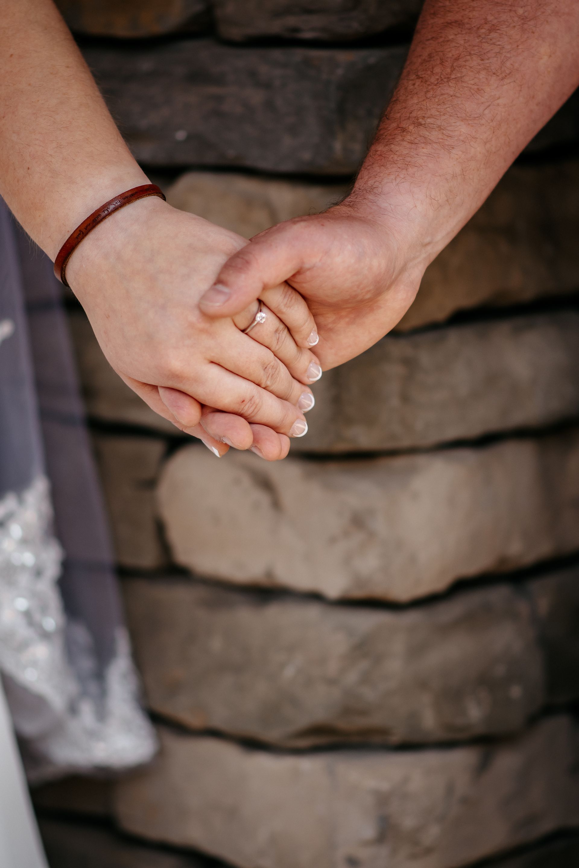 A bride and groom are holding hands in front of a stone wall.