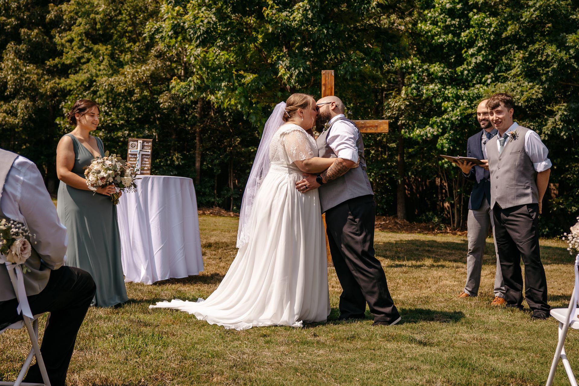 A bride and groom kissing at their wedding ceremony in front of a cross.