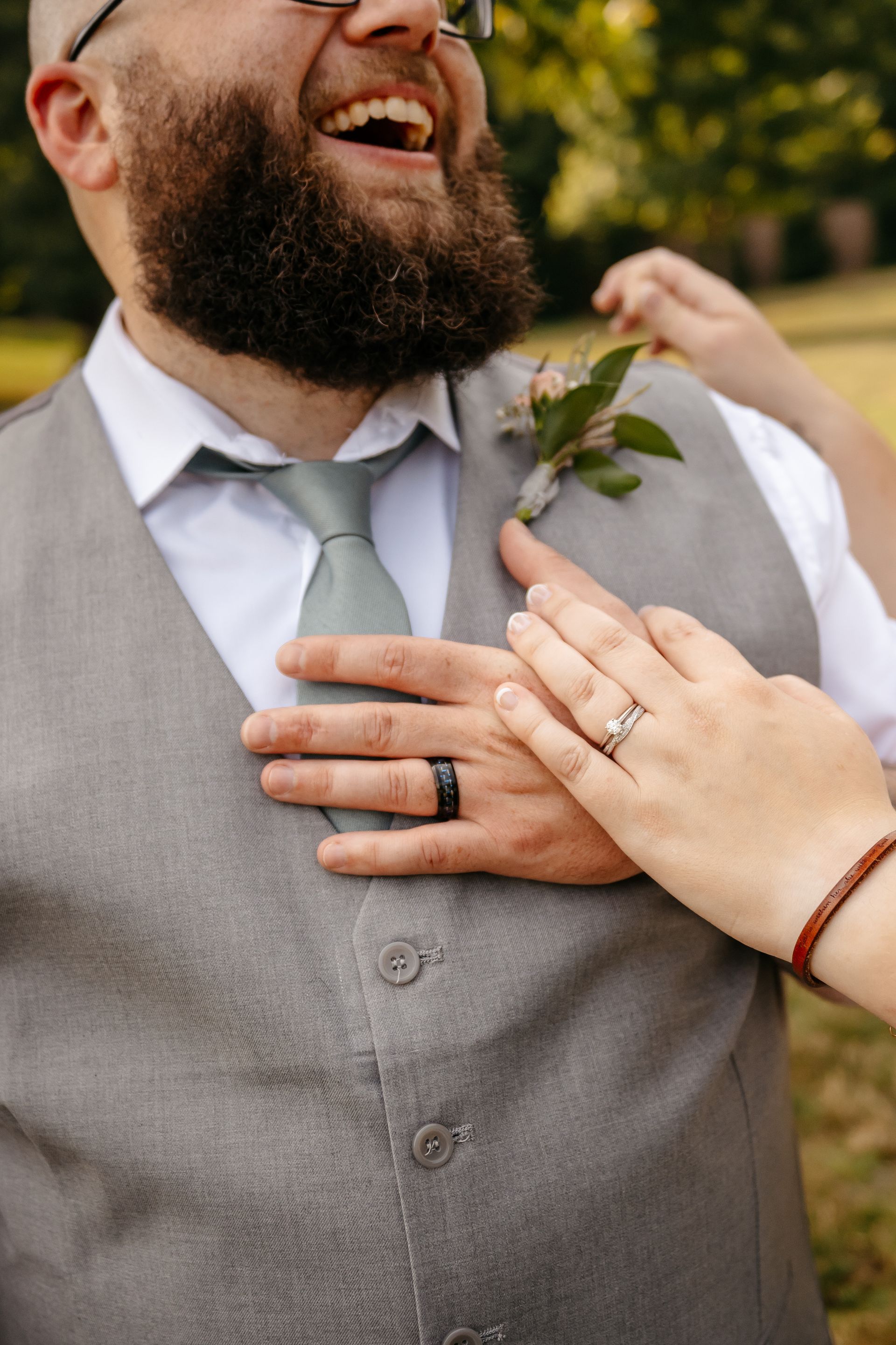A man with a beard and a tie is laughing while a woman holds his hand to his chest.