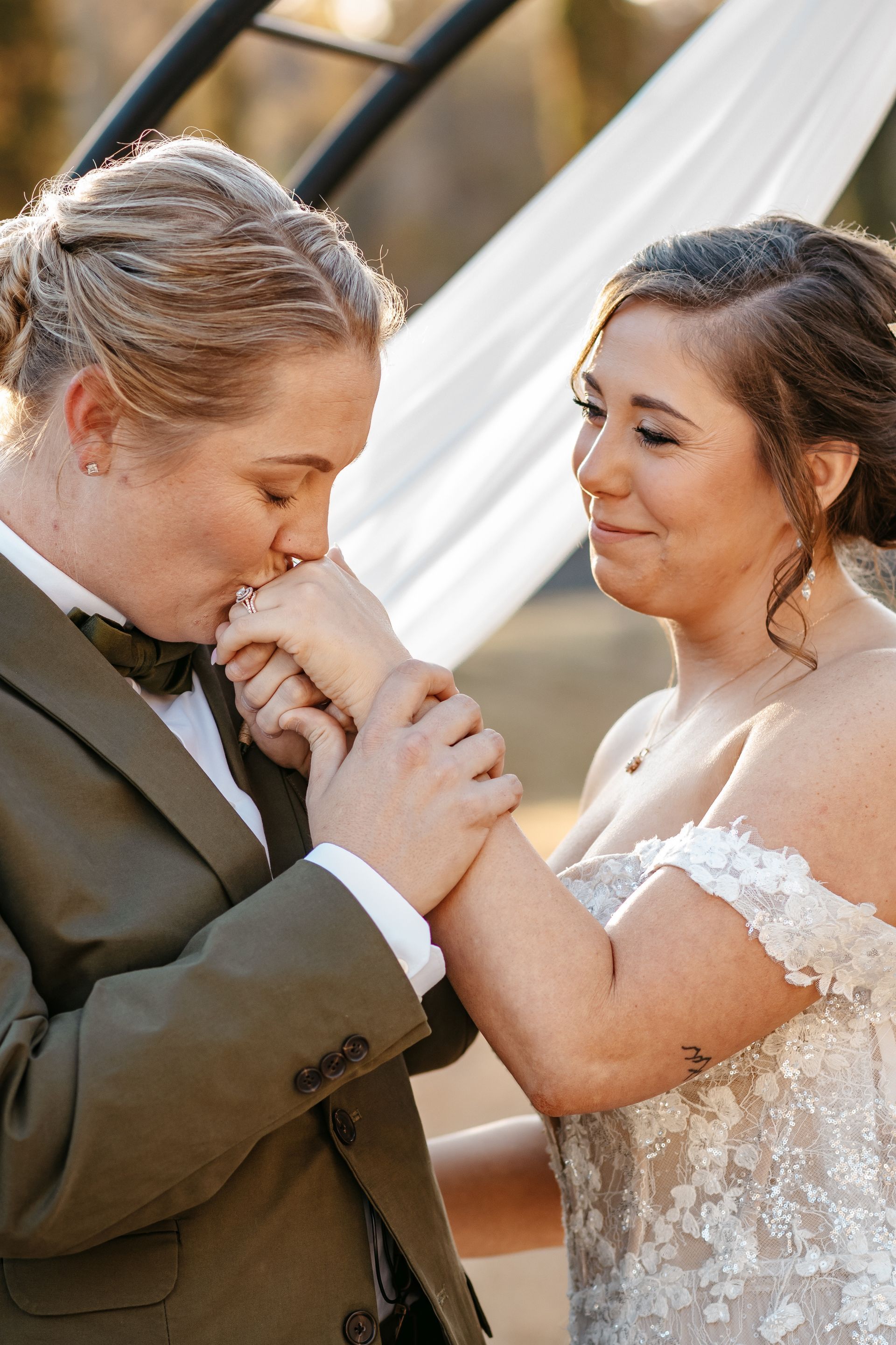 A bride and groom are kissing each other 's hands on their wedding day.