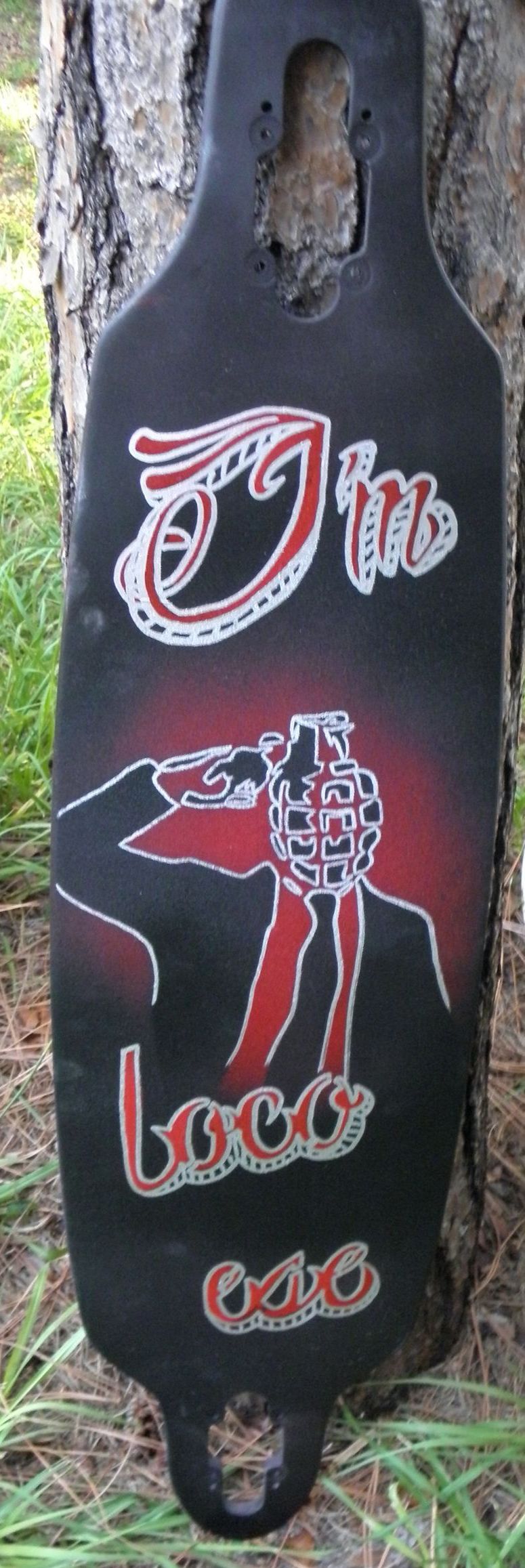 A black and red skateboard is leaning against a tree
