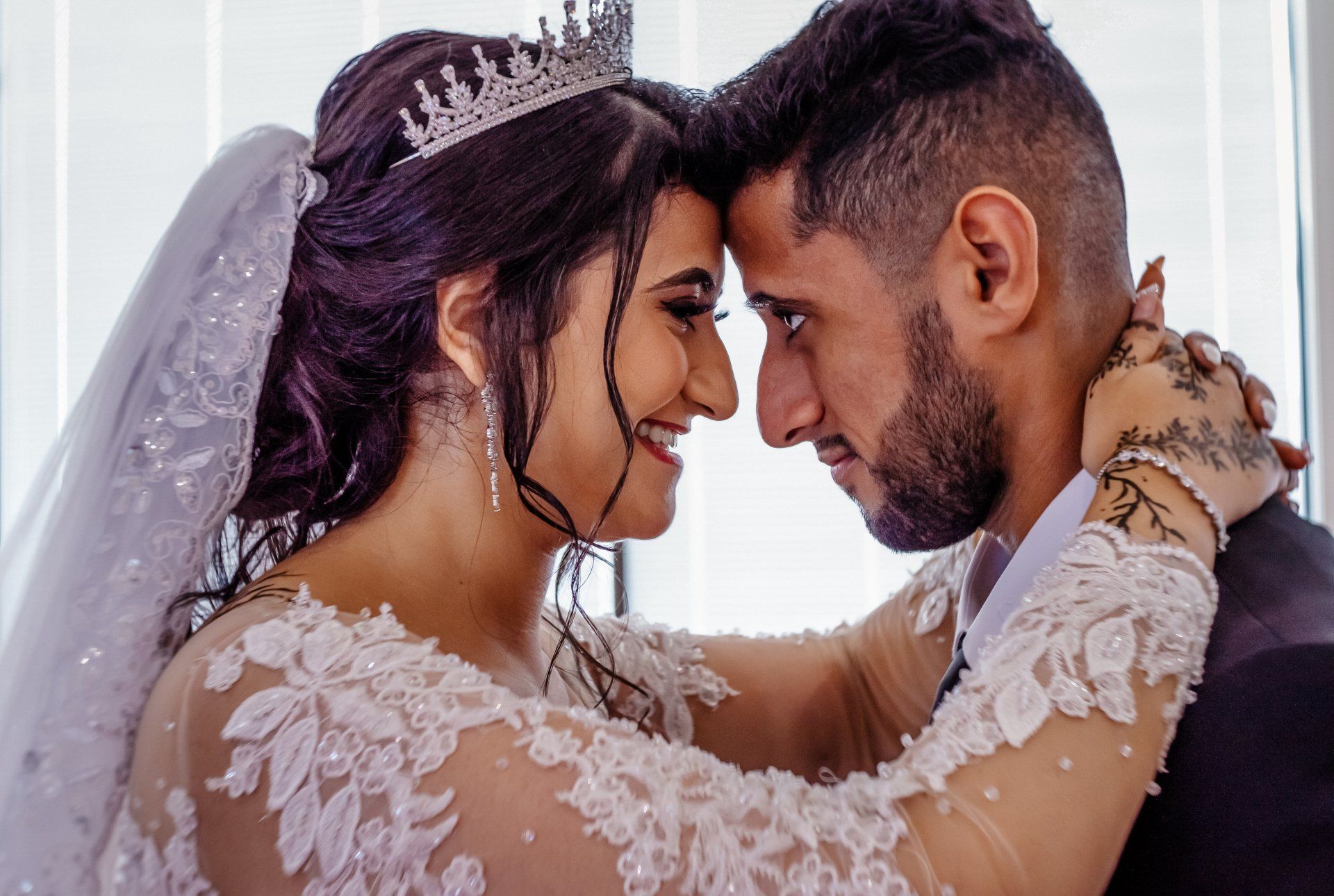 A bride and groom are hugging and looking at each other . the bride is wearing a tiara.