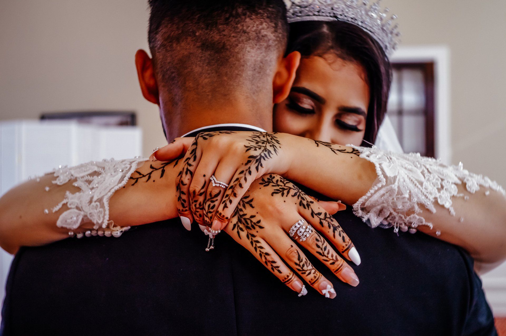 A bride with henna on her hands is hugging her groom.
