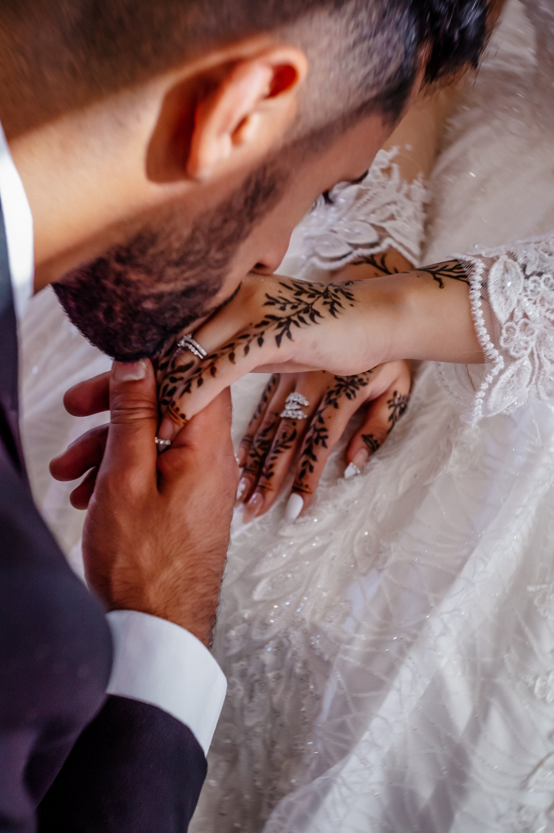 A bride and groom are kissing each other 's hands on their wedding day.