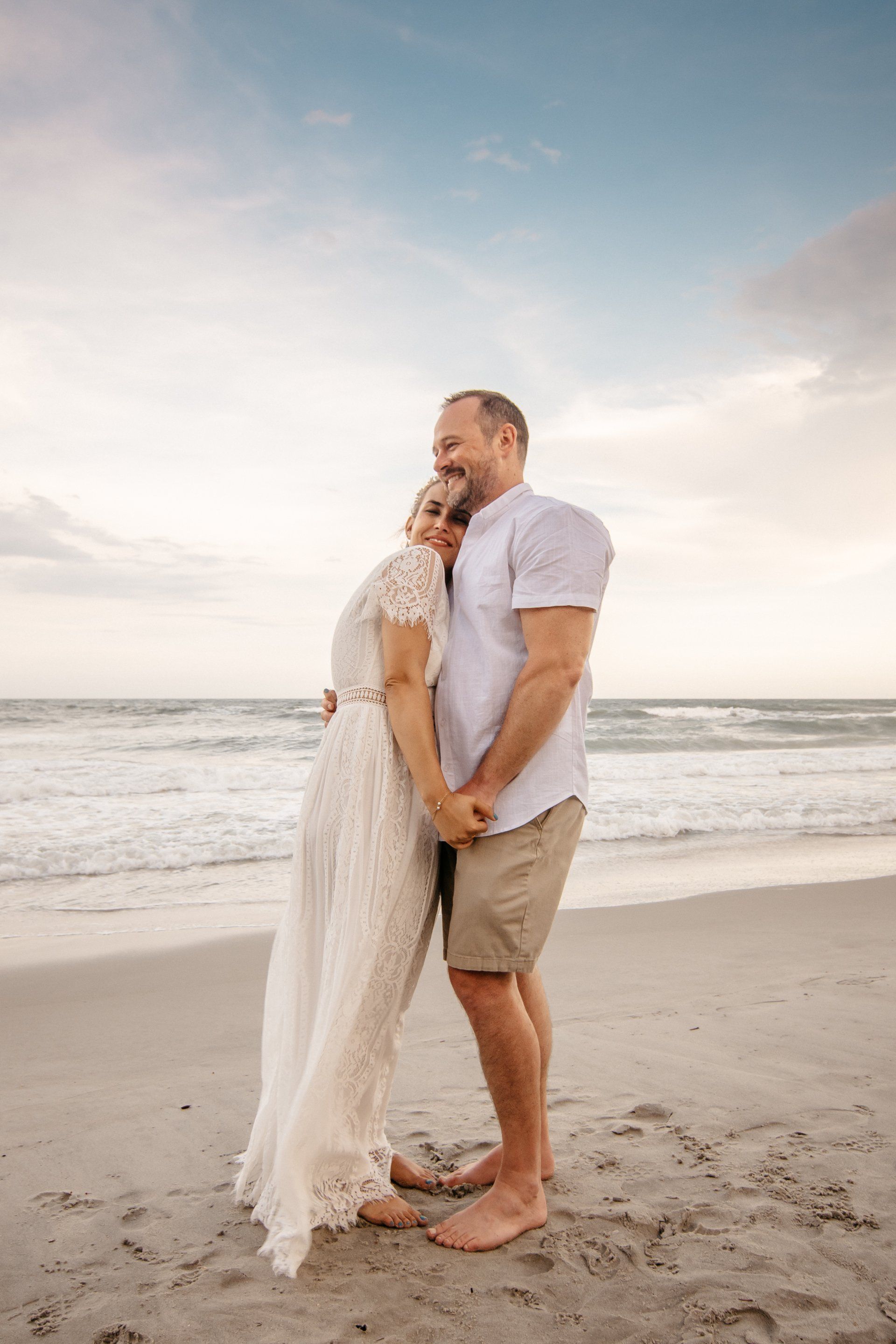 A man and a woman are standing on a beach holding hands.