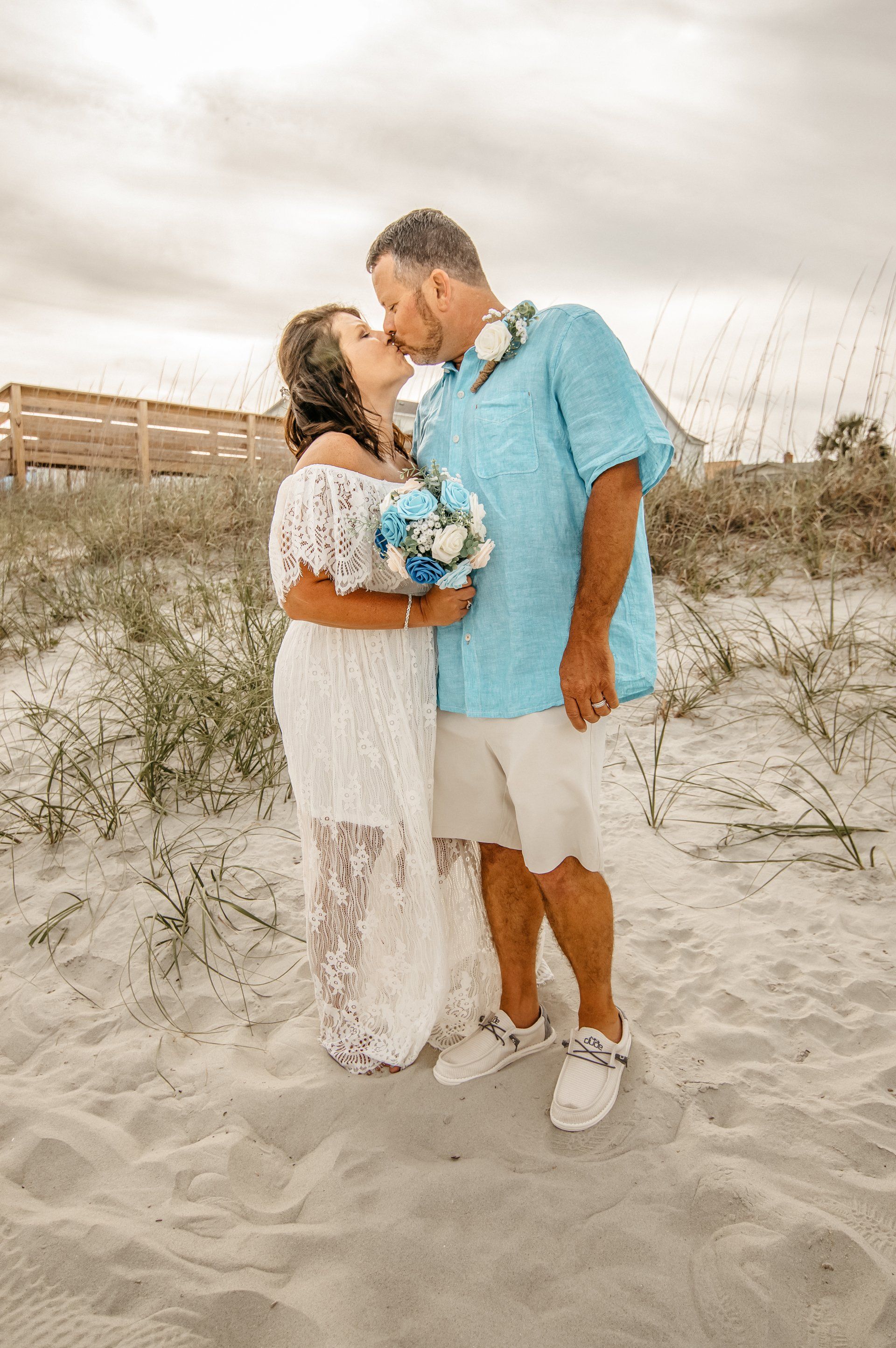 A bride and groom are kissing on the beach.