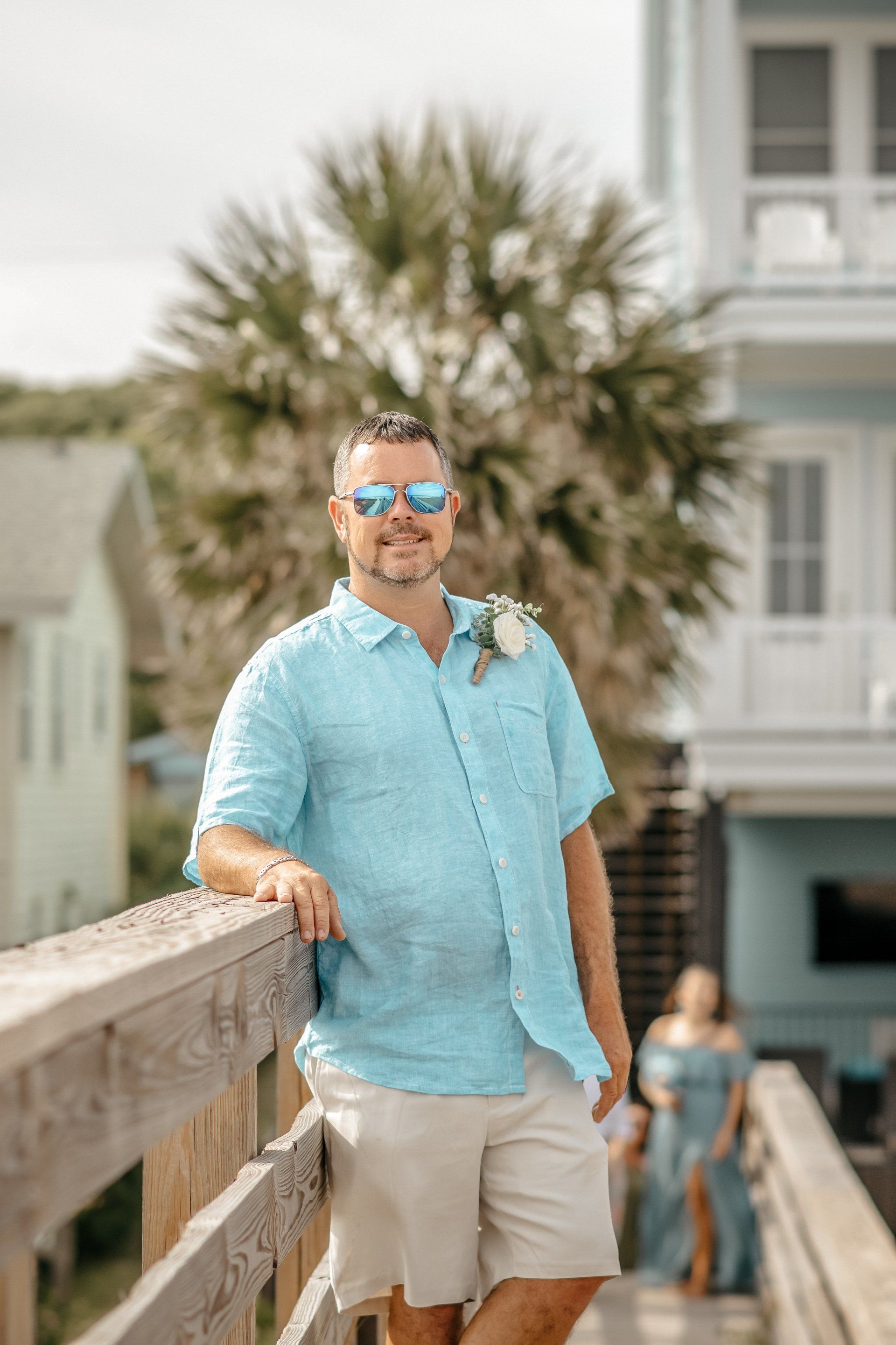 A man in a blue shirt and shorts is leaning on a railing.