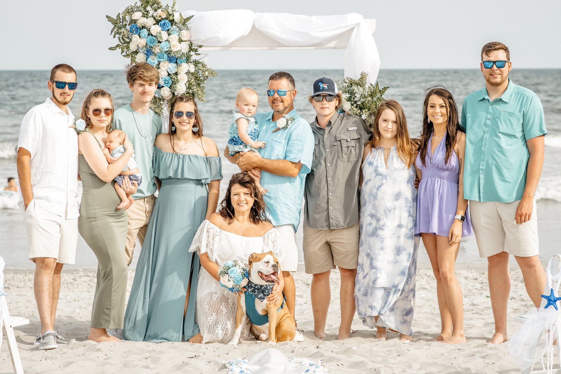A large family is posing for a picture on the beach.