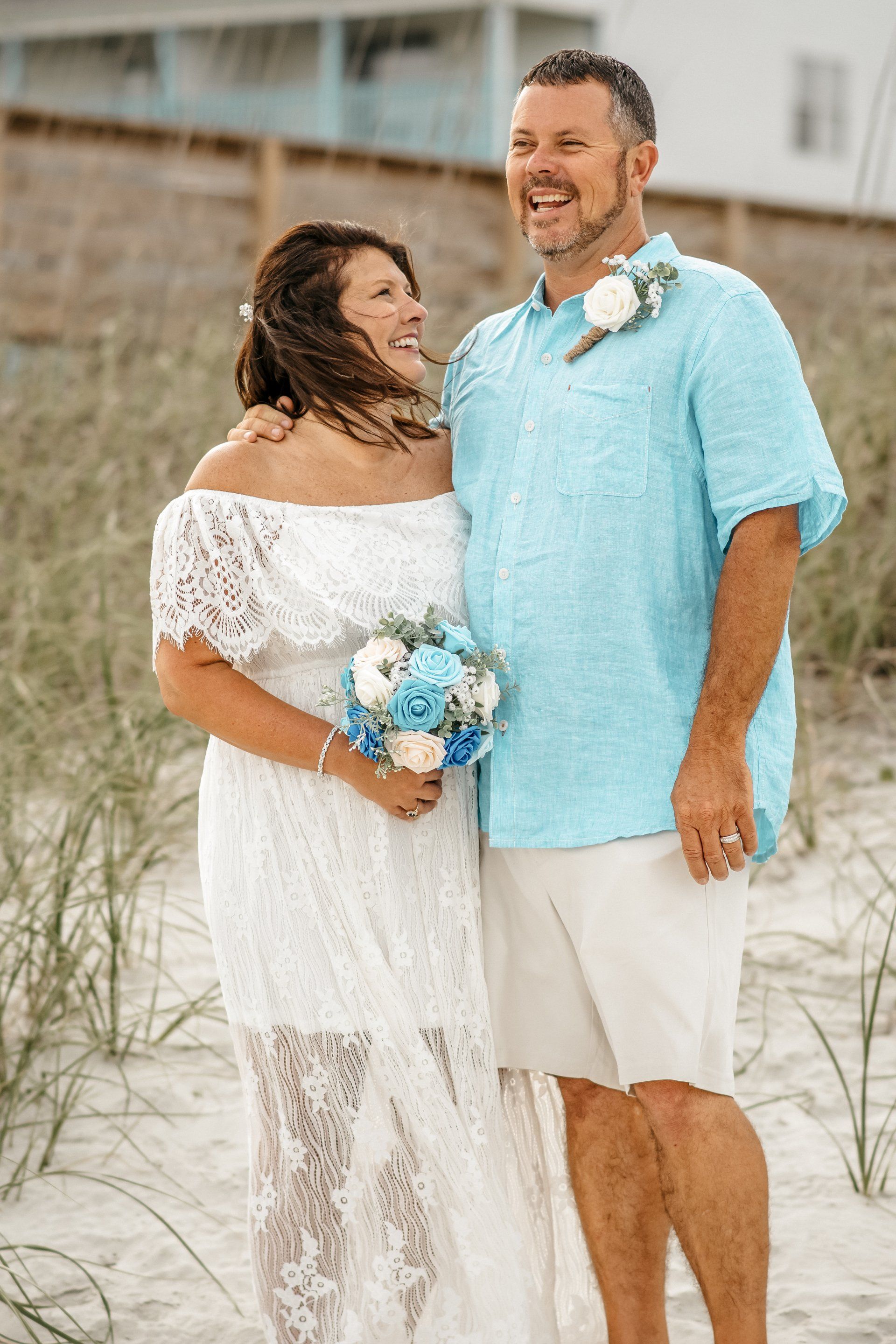 A bride and groom are posing for a picture on the beach.